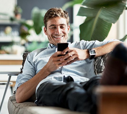 Person smiling on a couch while looking at a smartphone in a bright indoor living room.