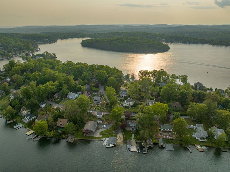 Aerial view of a lakeside neighborhood with trees, docks, and a large island at sunset.