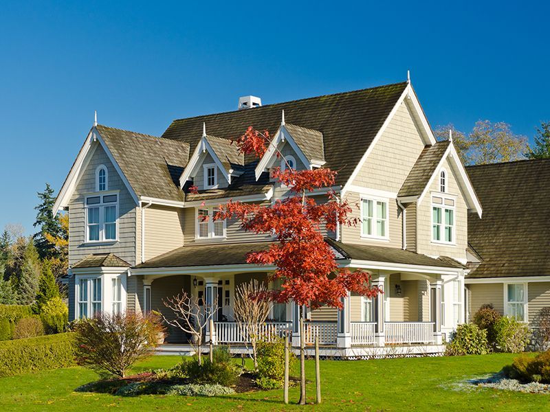 Large beige suburban house with white trim, red dormer windows, and a porch under a clear blue sky