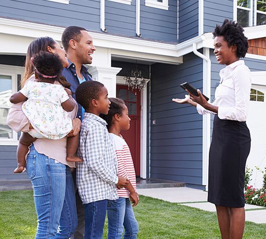 Family meeting with a real estate agent outside a blue house while holding a clipboard