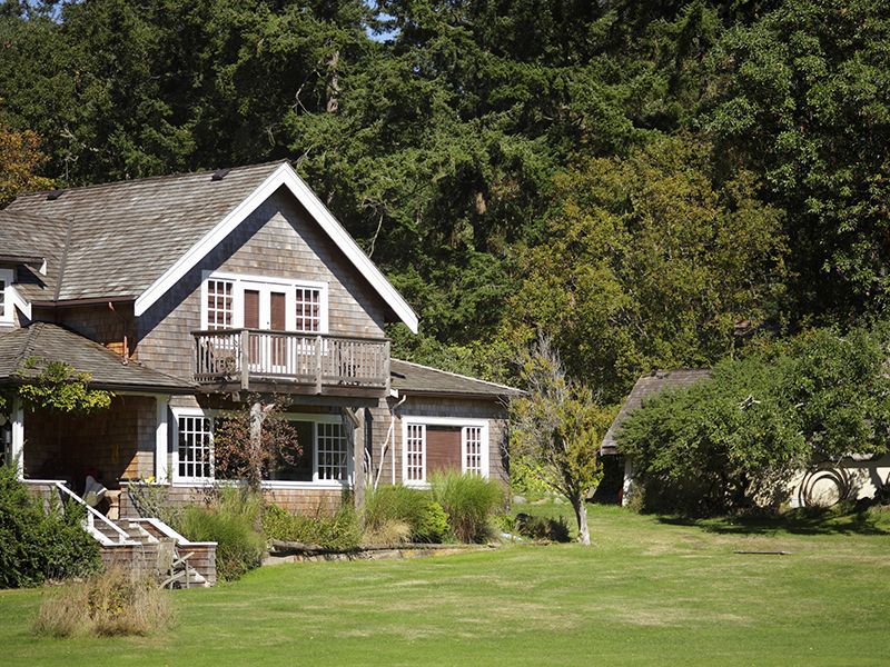 Small house with white trim and brown roof beside a large green lawn and trees