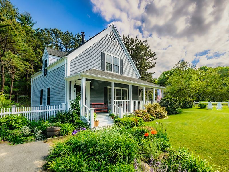 White farmhouse with front porch, green lawn, and landscaped garden under a blue sky
