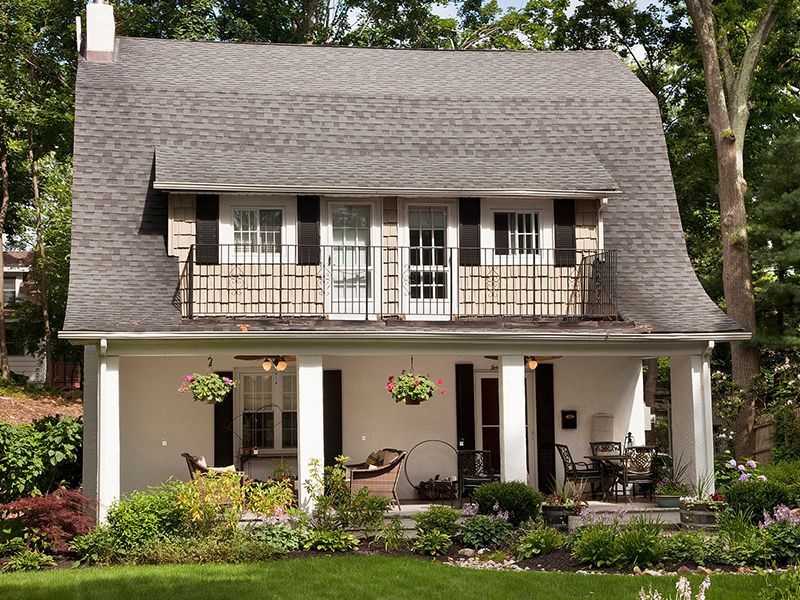 White two-story cottage with a steep roof, porch, and flower-filled front yard
