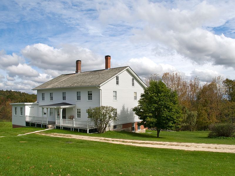 White farmhouse with porch on a green lawn under a cloudy sky