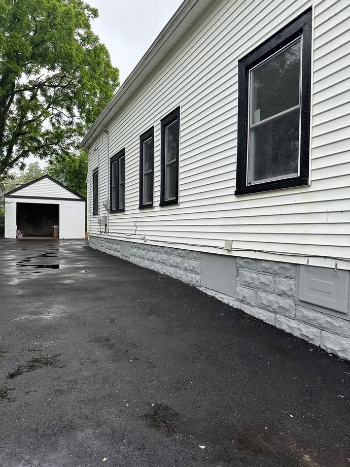 Side of a white house with black-trimmed windows and a detached garage on a wet asphalt driveway