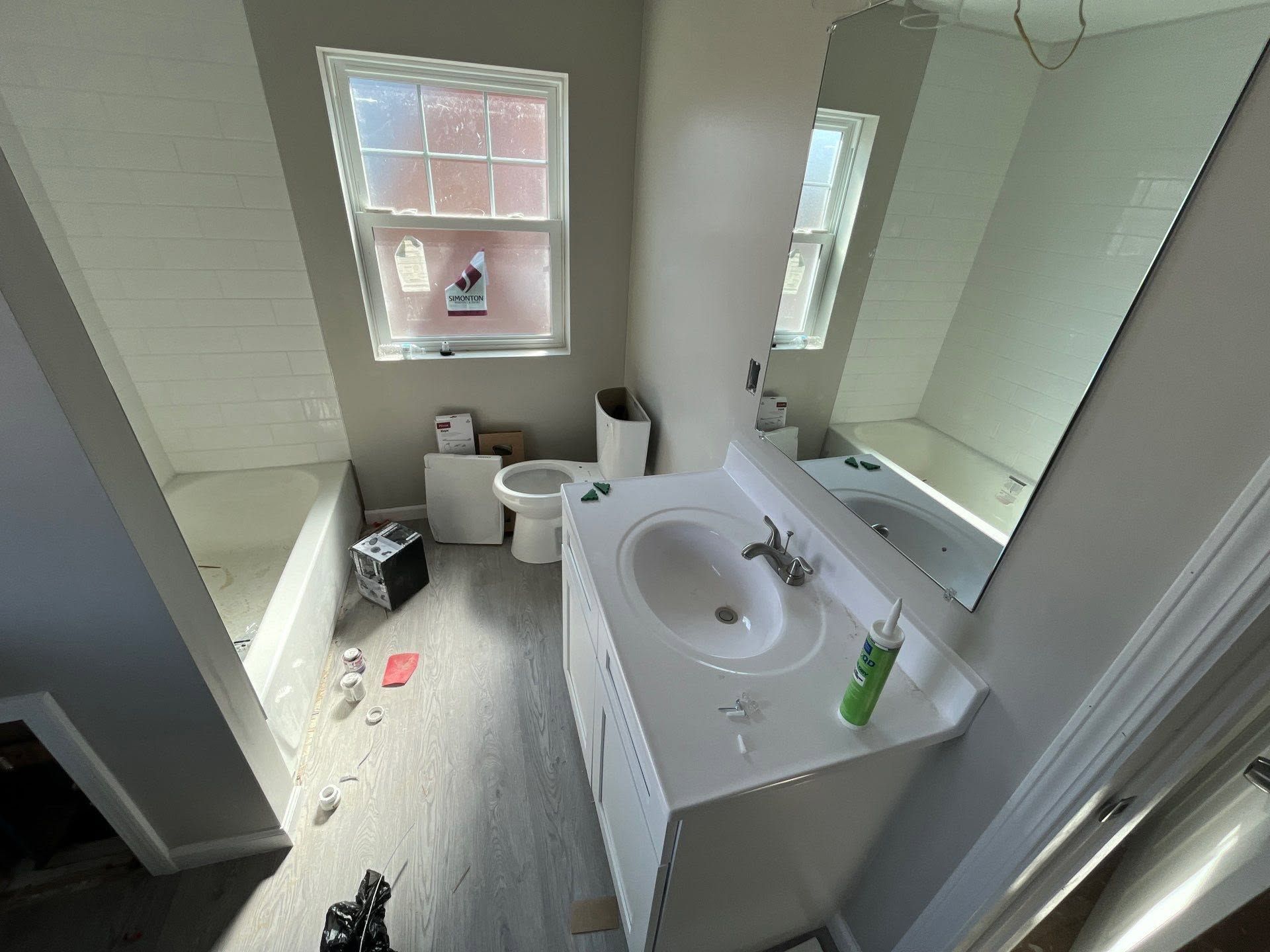 Small bathroom with white sink vanity, toilet, window, and mirror; clutter on the floor.