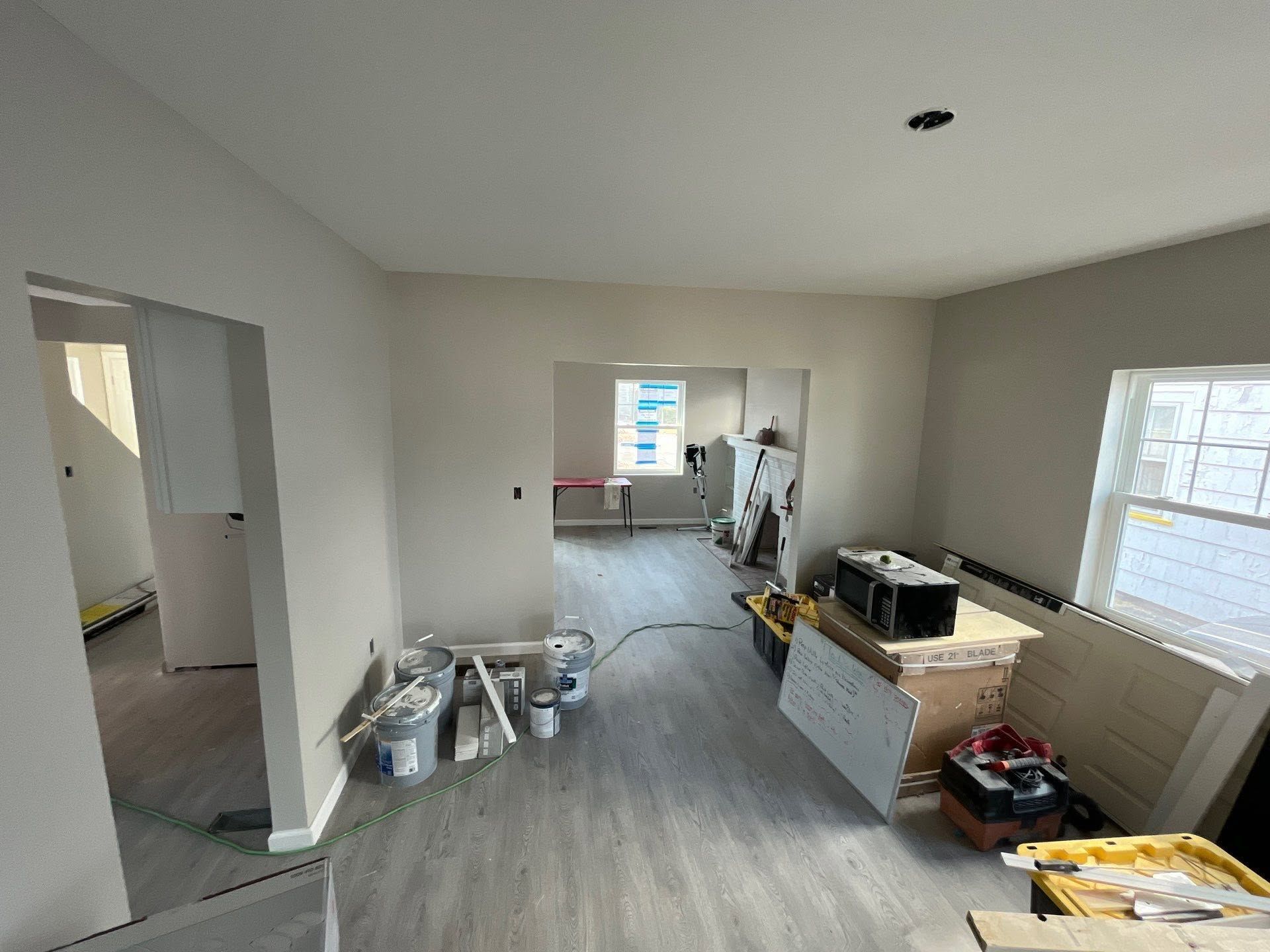 Empty room under renovation with paint supplies, gray carpet, and boxes near windows.