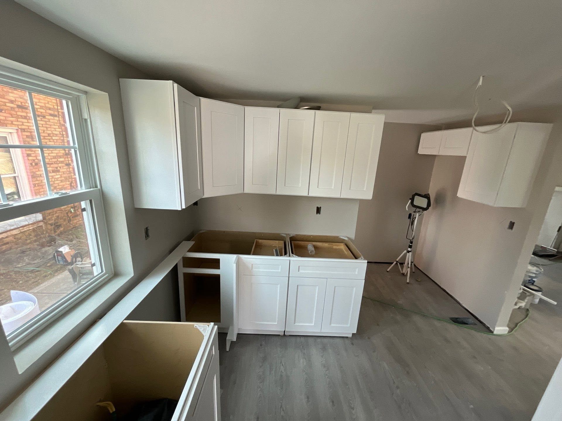Small kitchen under renovation with white cabinets, unfinished counters, and gray flooring