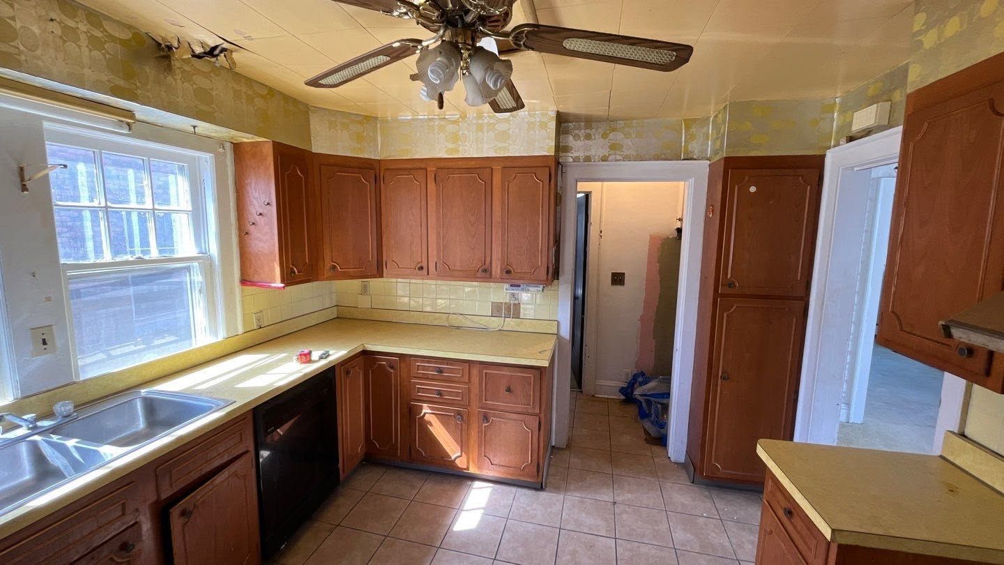 Empty kitchen with wooden cabinets, yellow countertops, ceiling fan, and a window over the sink.