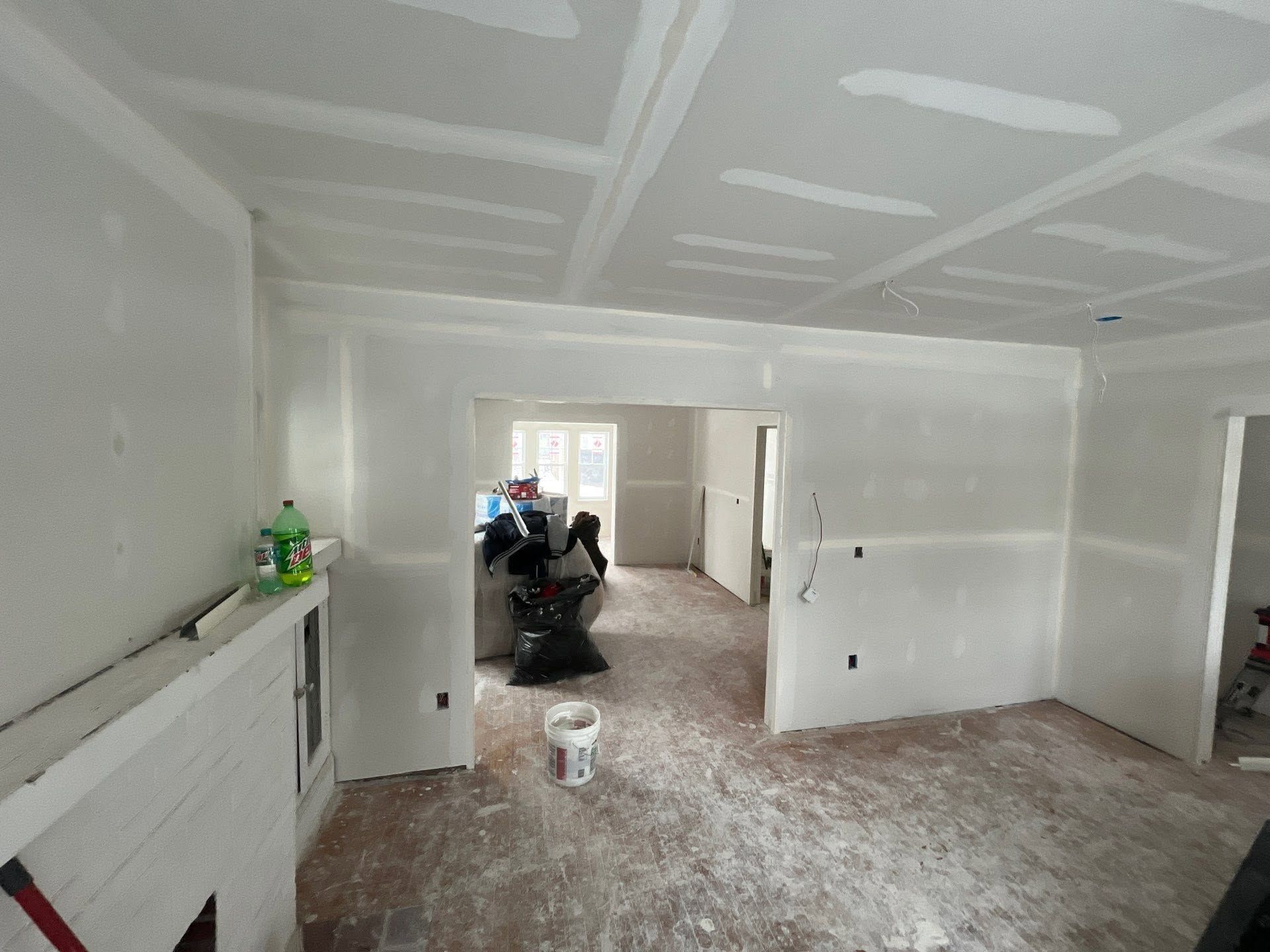 Renovated room with white walls and ceiling, drywall seams visible, and construction materials on the floor.