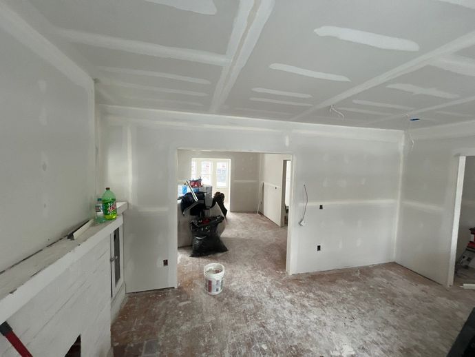 Renovated room with white walls and ceiling, drywall seams visible, and construction materials on the floor.