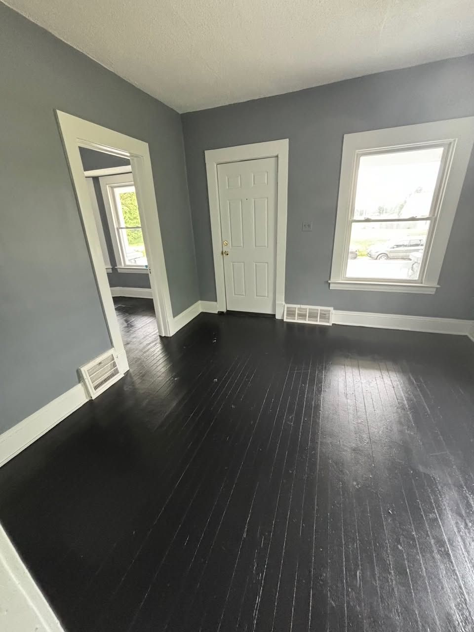 Empty room with dark wood floors, gray walls, white trim, and two windows with a doorway.