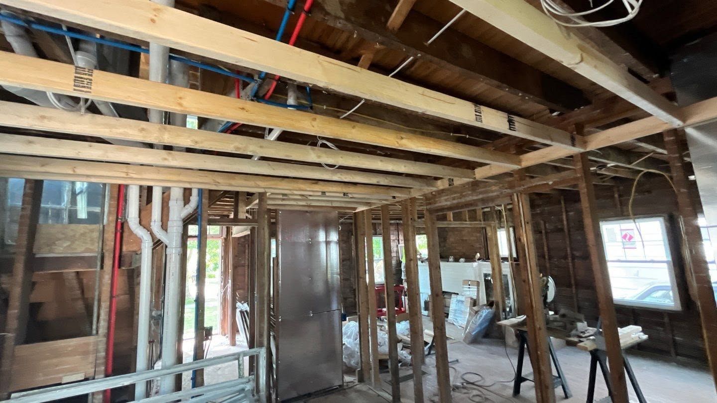 Exposed wooden framing inside a building under construction, with open wall studs and ceiling joists.