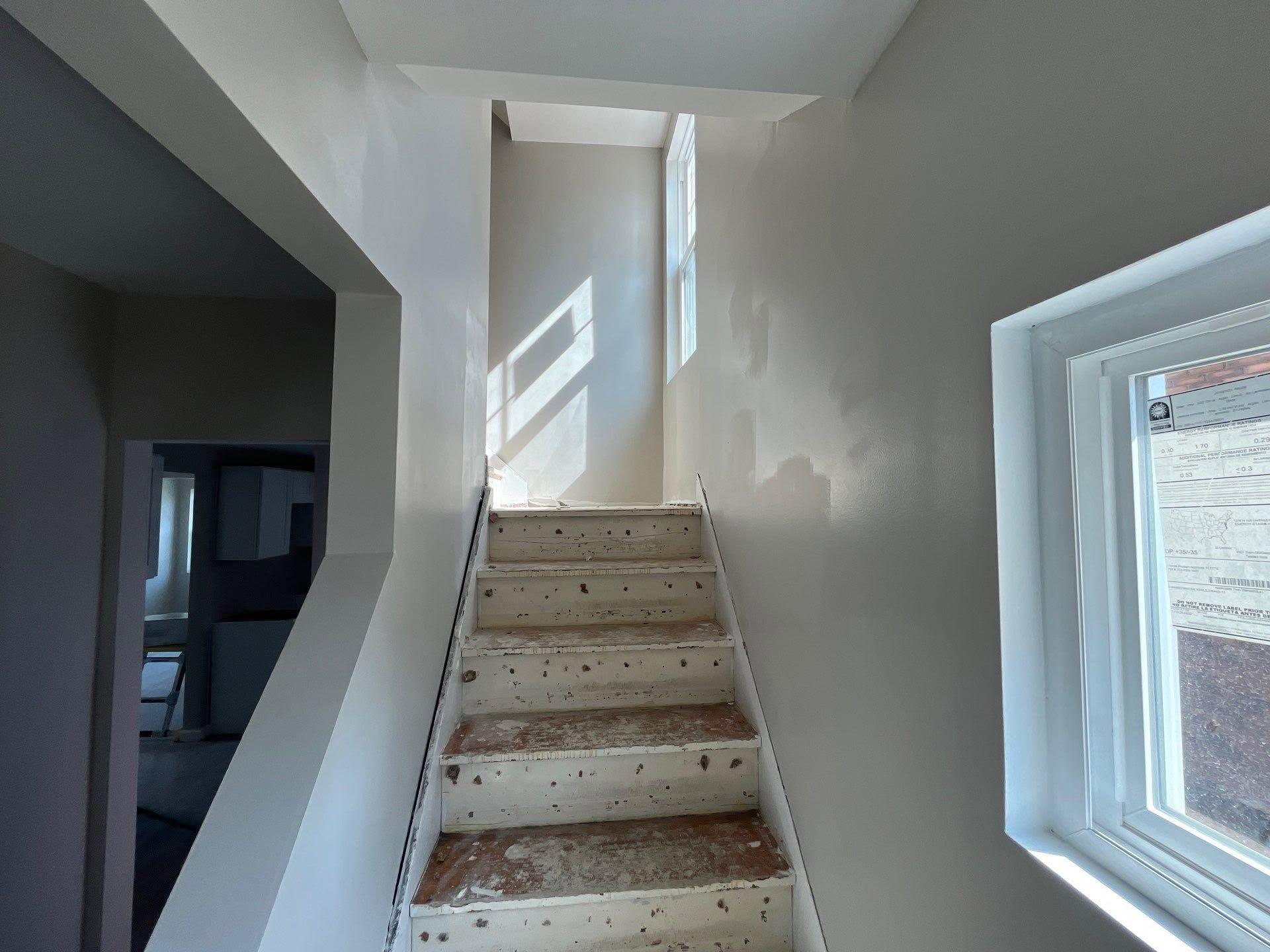 Interior staircase with carpeted steps, white walls, and a window letting in sunlight.