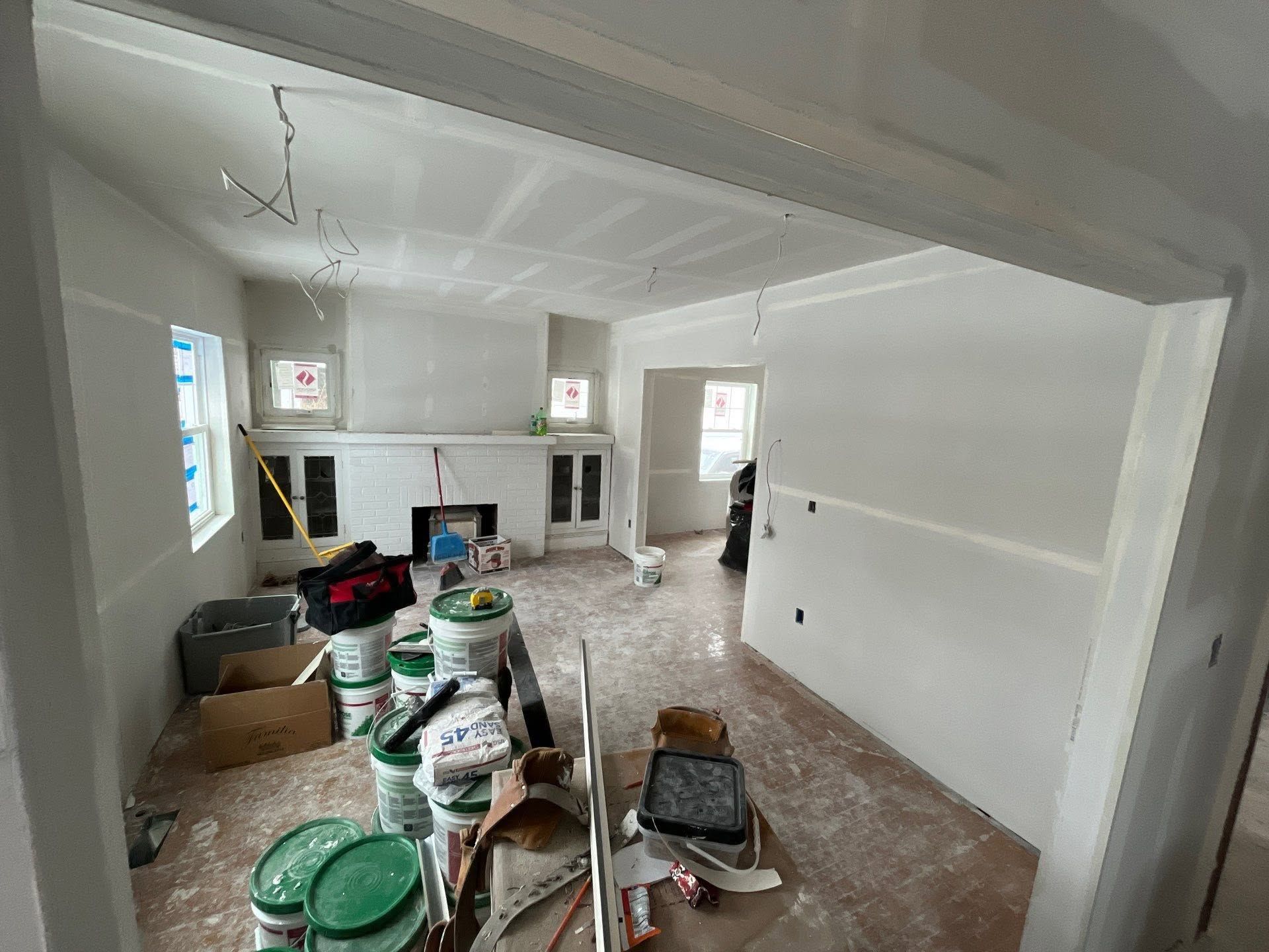 Renovation in progress in a bright living room with paint buckets, tools, and covered floors