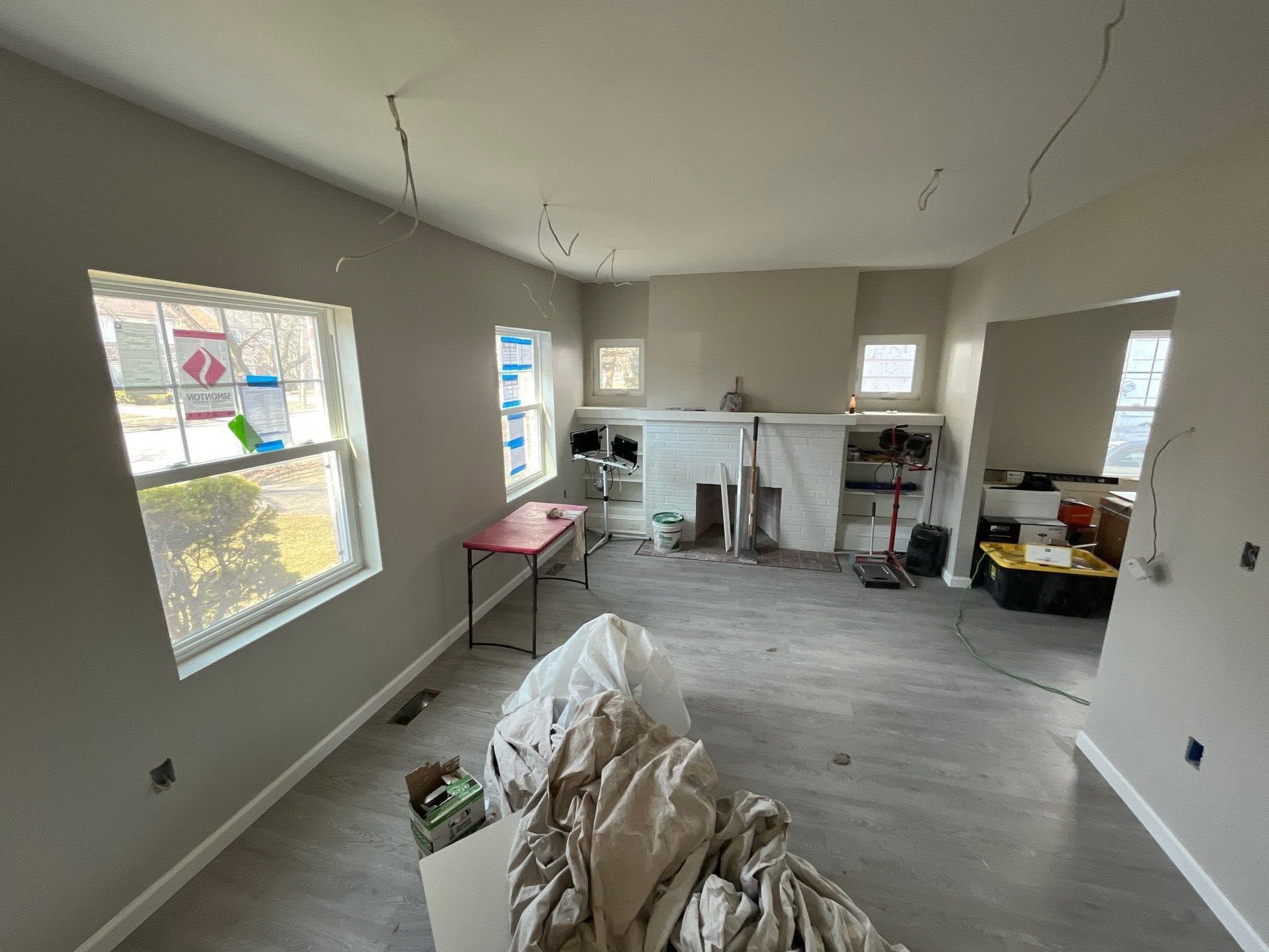Empty unfinished room with gray floors, white walls, windows, tools, and construction materials.
