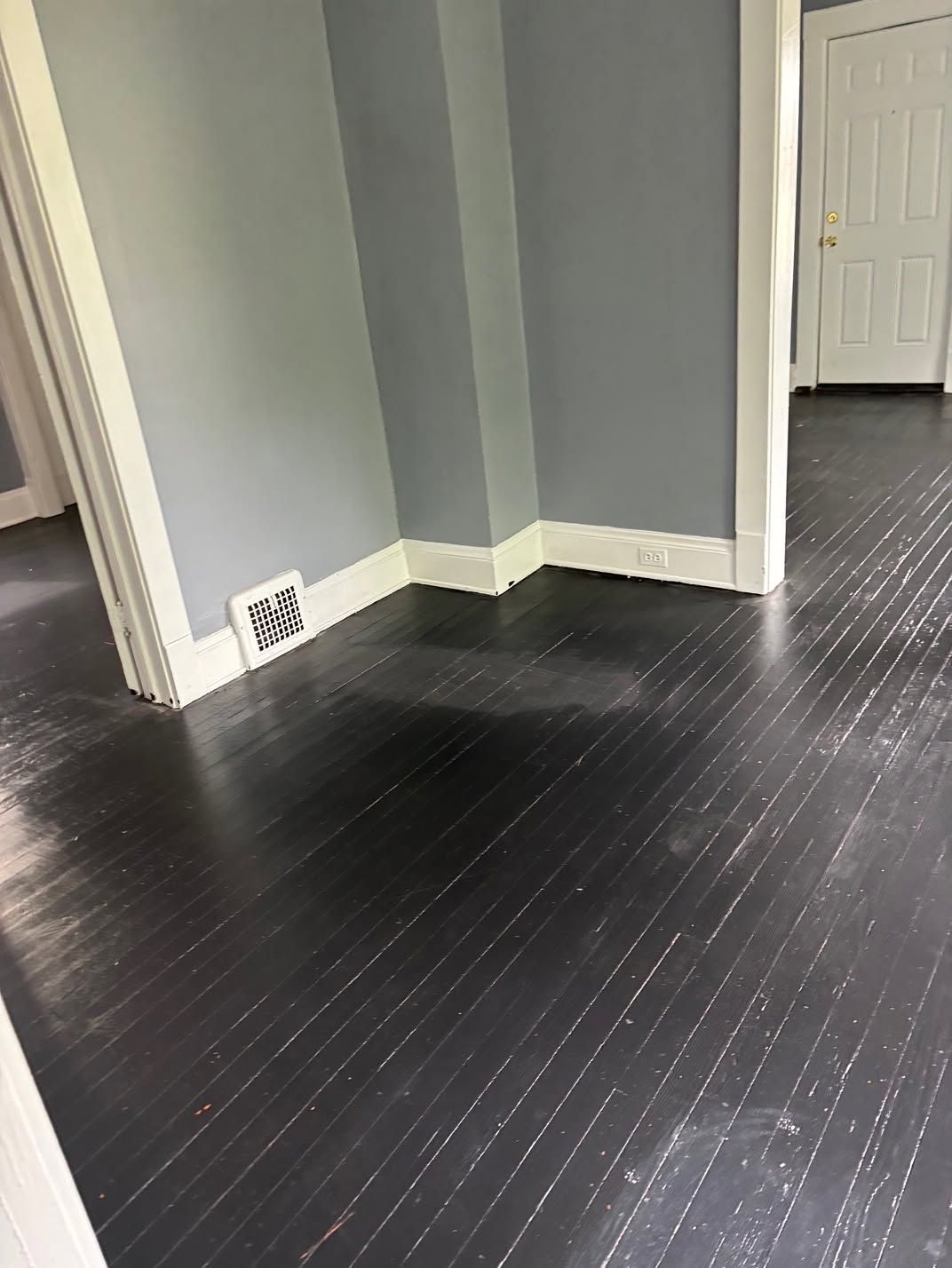 Empty room corner with dark wood floor, gray walls, and white trim near a doorway.