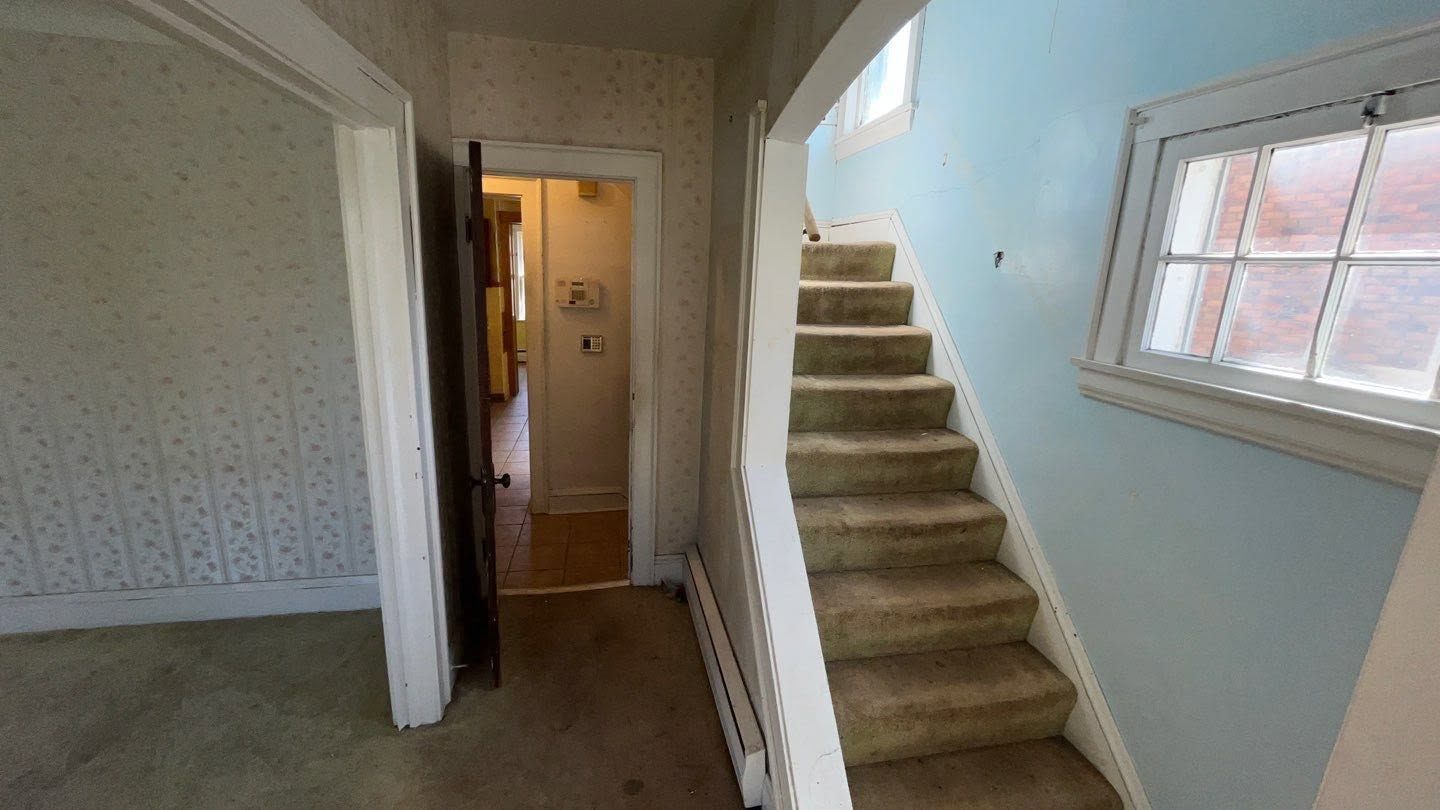 Interior hallway with carpeted stairs, a doorway, and a window on the right