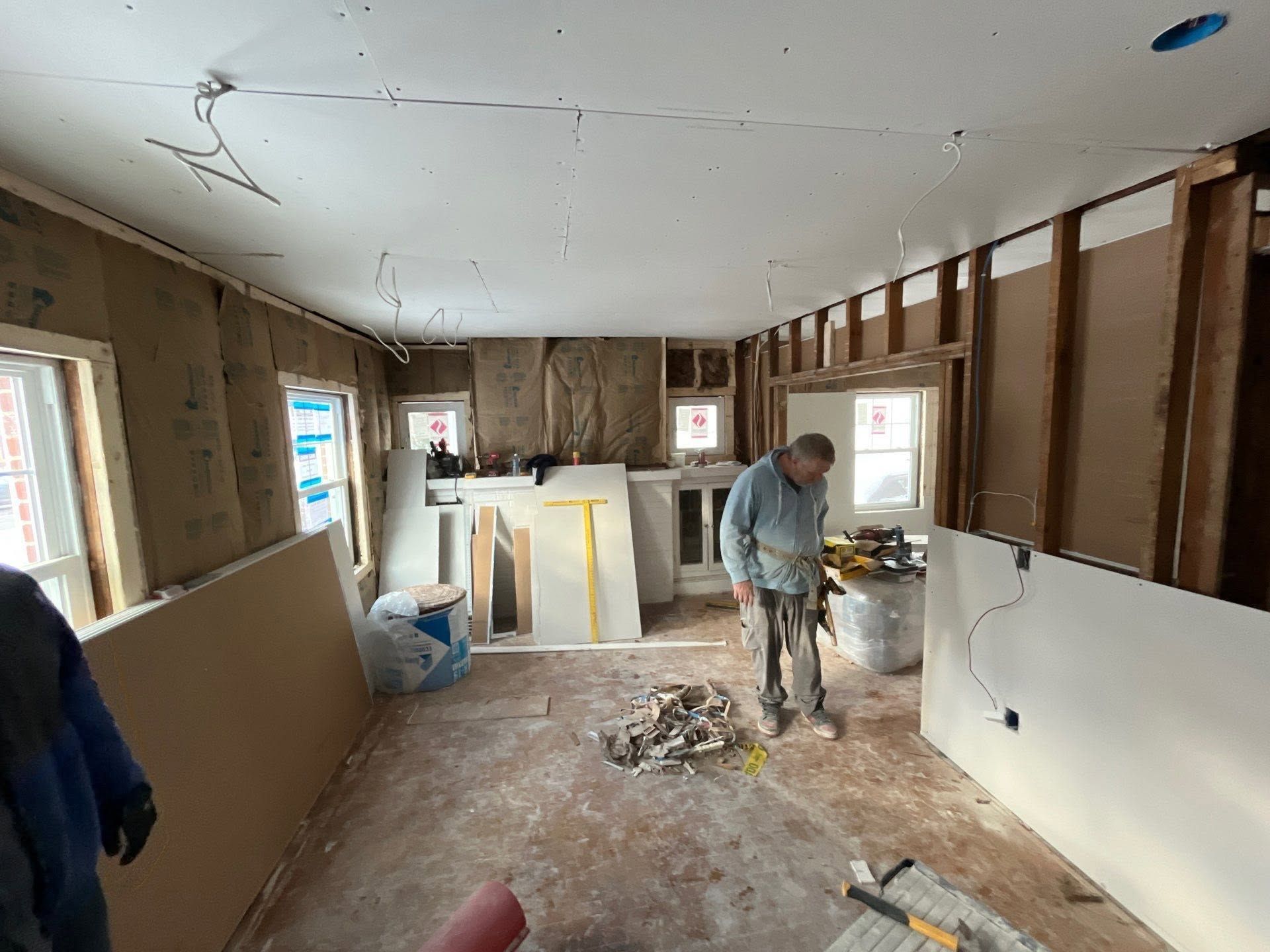 Home renovation scene with worker in dusty room, exposed walls, and unfinished ceiling