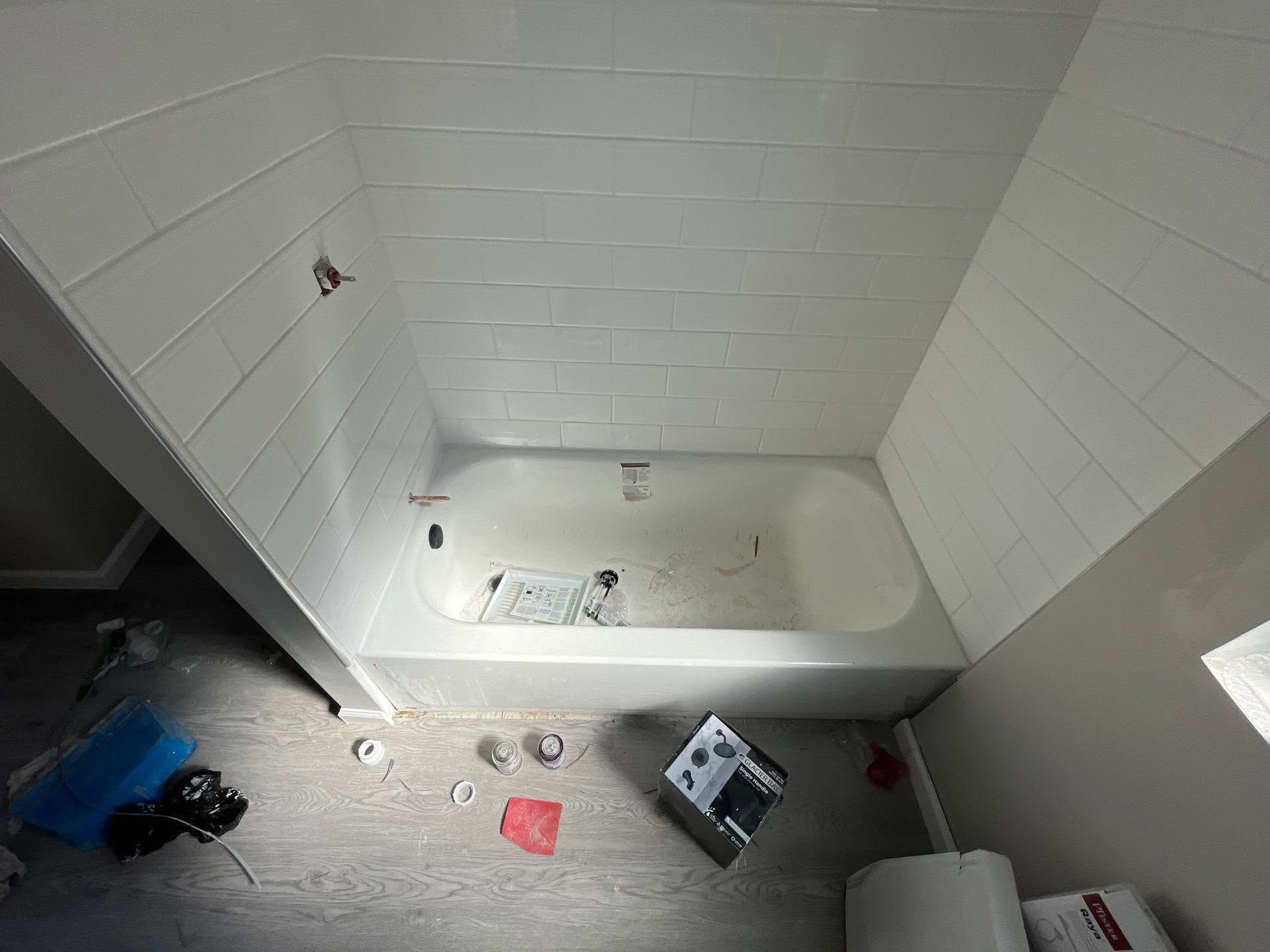 Empty white bathtub in a small bathroom with debris scattered on the floor.