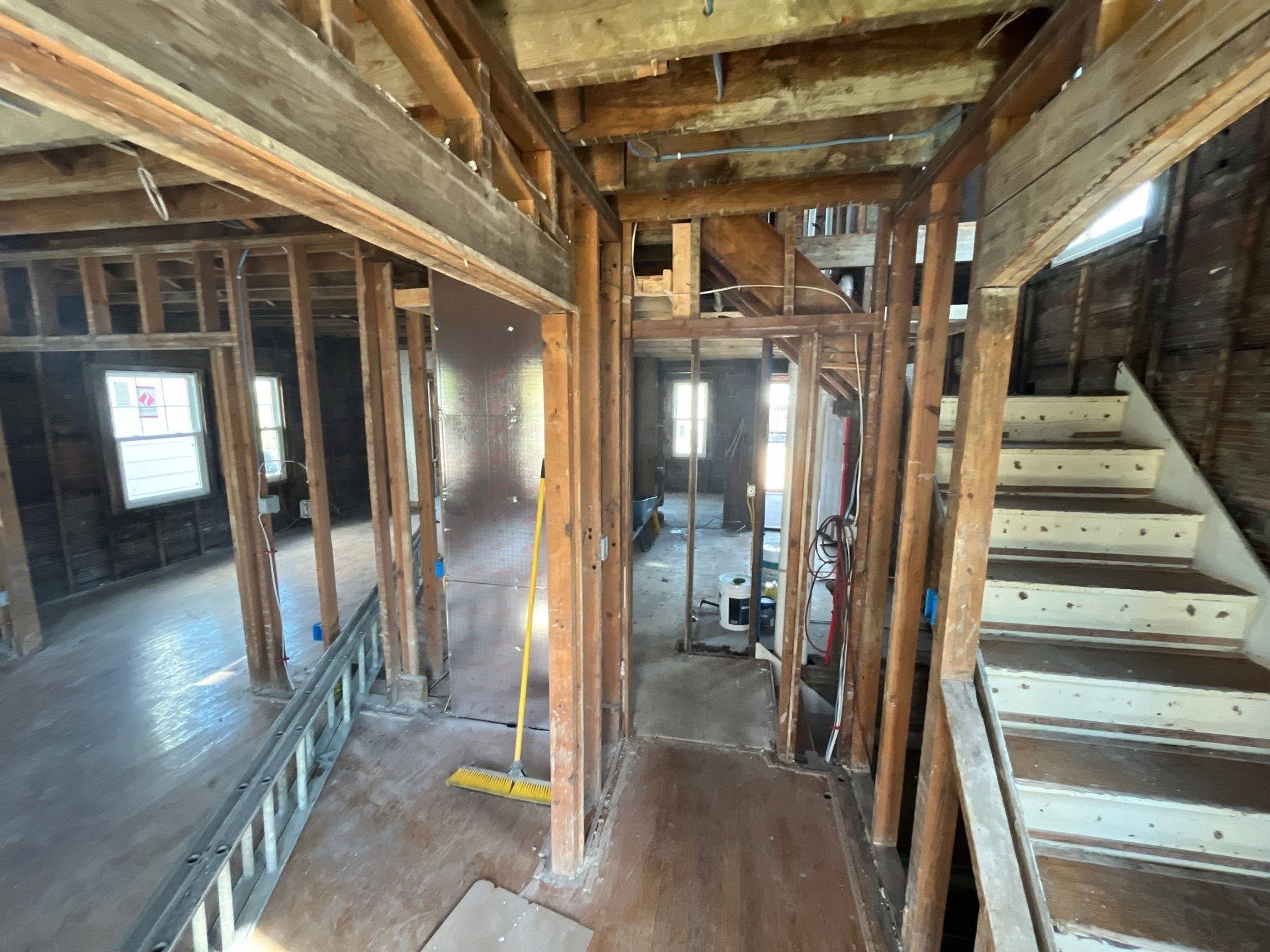 Interior of a partially renovated house with exposed framing, wooden stairs, and unfinished floors.