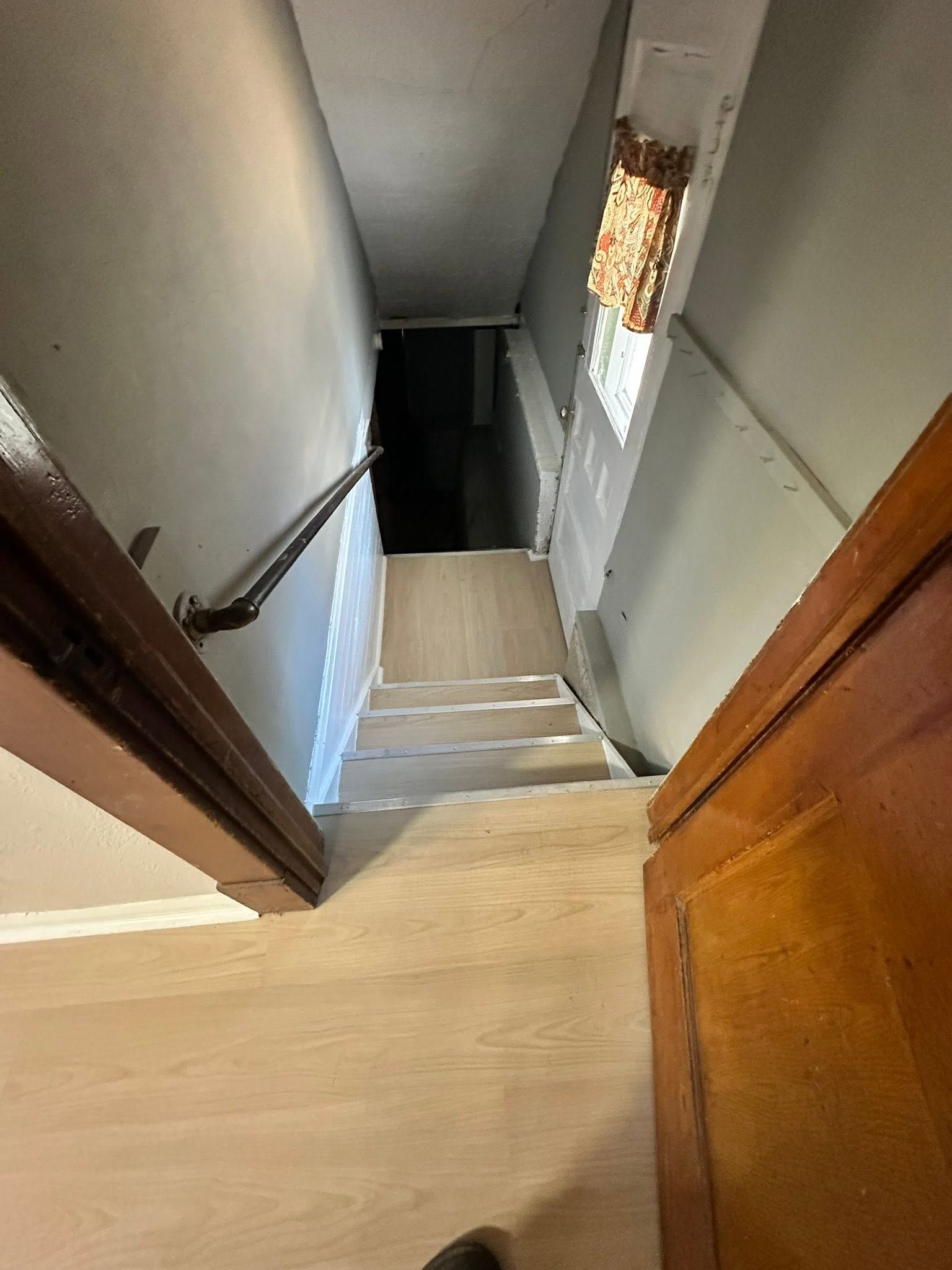 Top of a narrow indoor stairway with beige walls, wood trim, and a window at the landing.