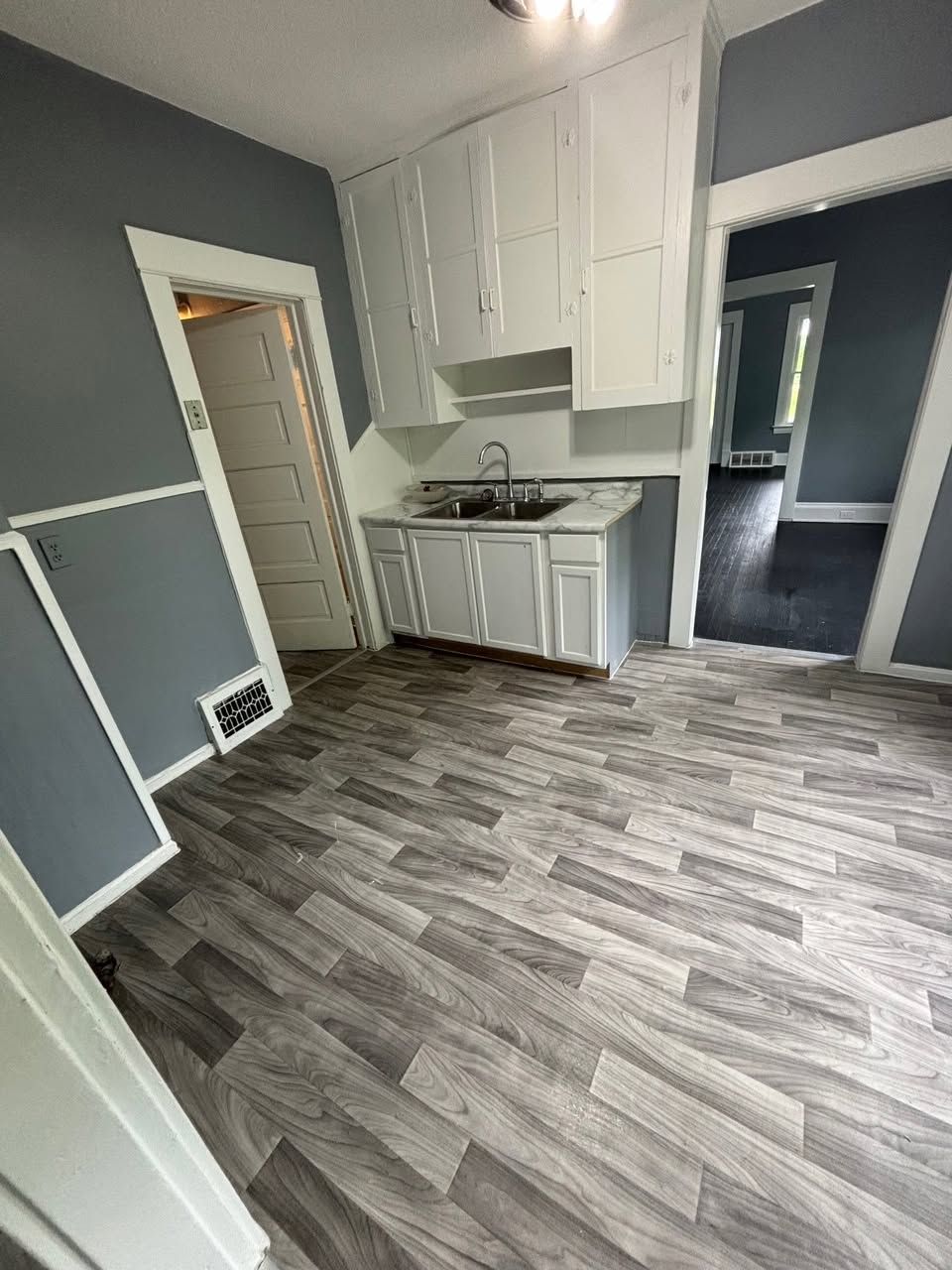 Small kitchen with white cabinets, gray walls, and wood-look flooring.