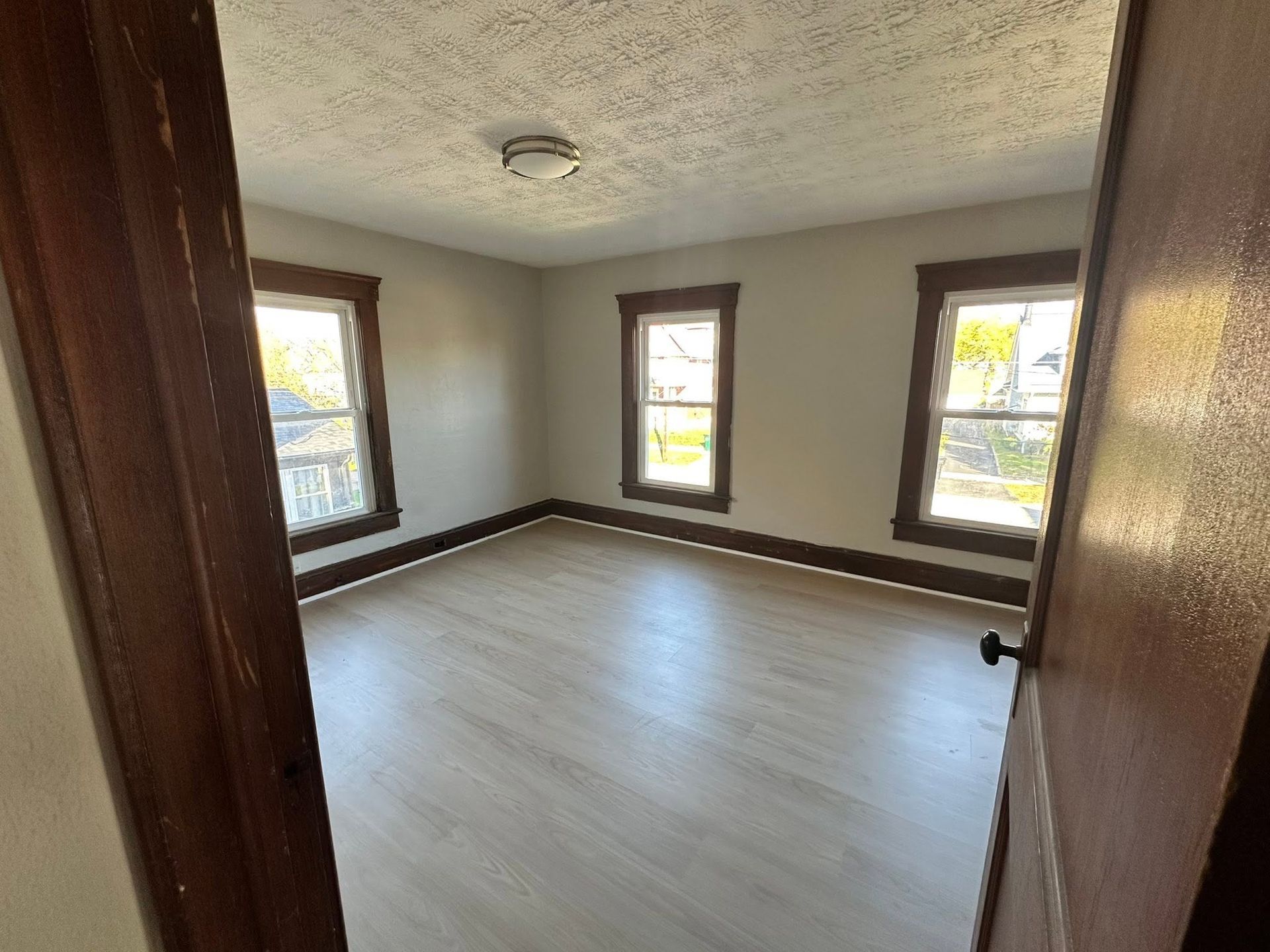 Empty gray room with white flooring, dark trim, and three windows letting in daylight