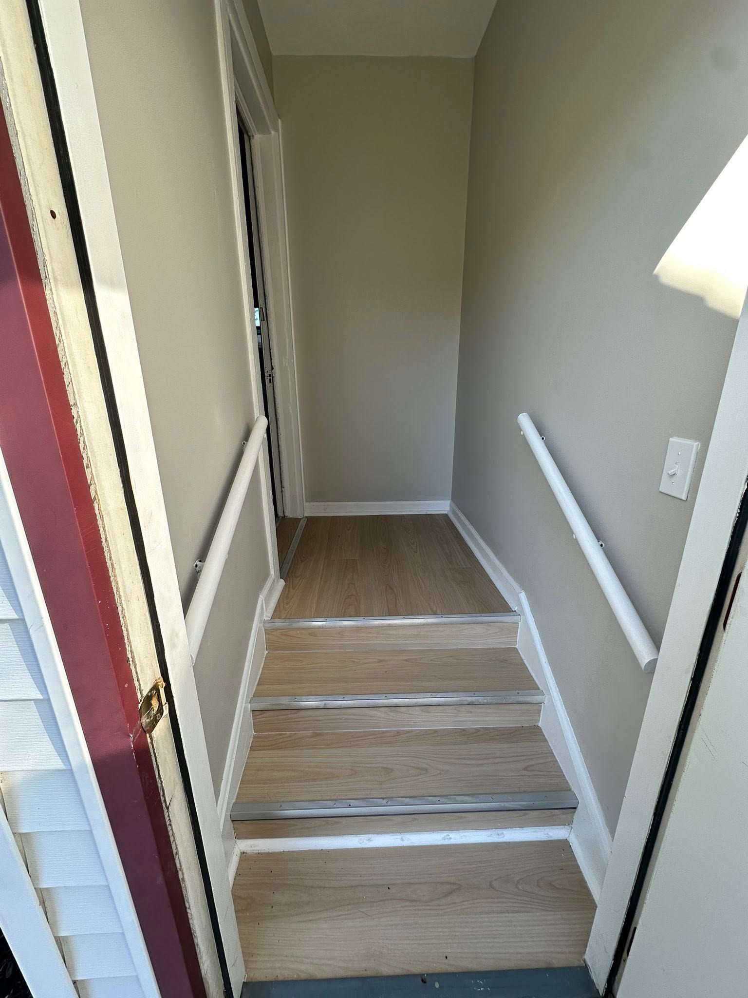 Narrow indoor stairway with wood steps, white handrails, and a door at the top