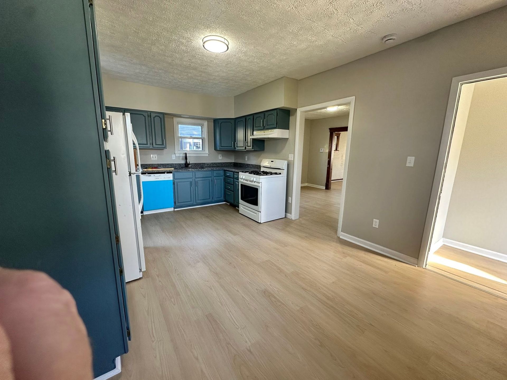 Empty kitchen and dining area with blue cabinets, white stove, and wood-look flooring