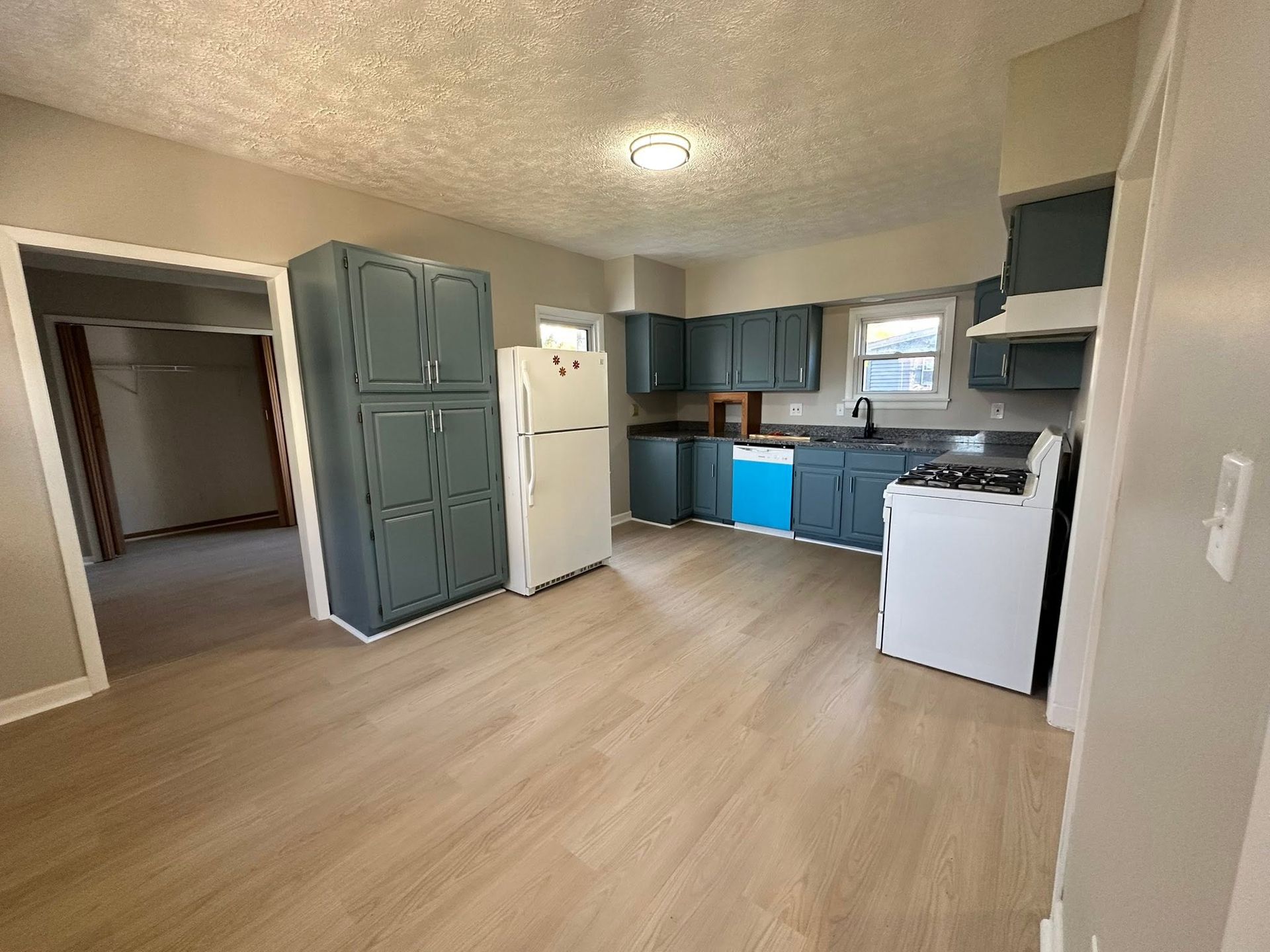 Empty kitchen with blue cabinets, light wood floors, and a white stove in a small apartment.