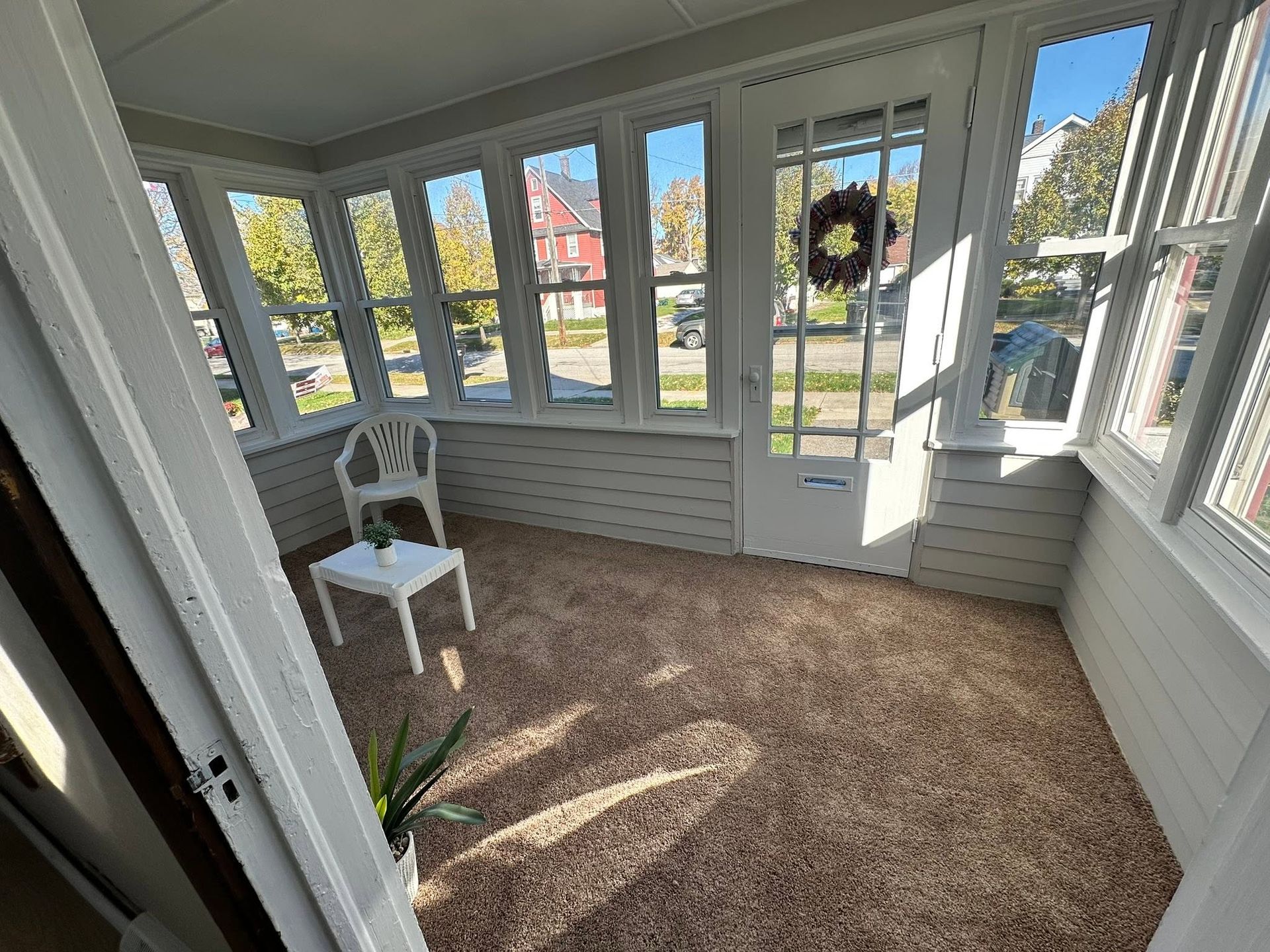 Sunroom with large windows, a white chair, and a wreath on the glass door.