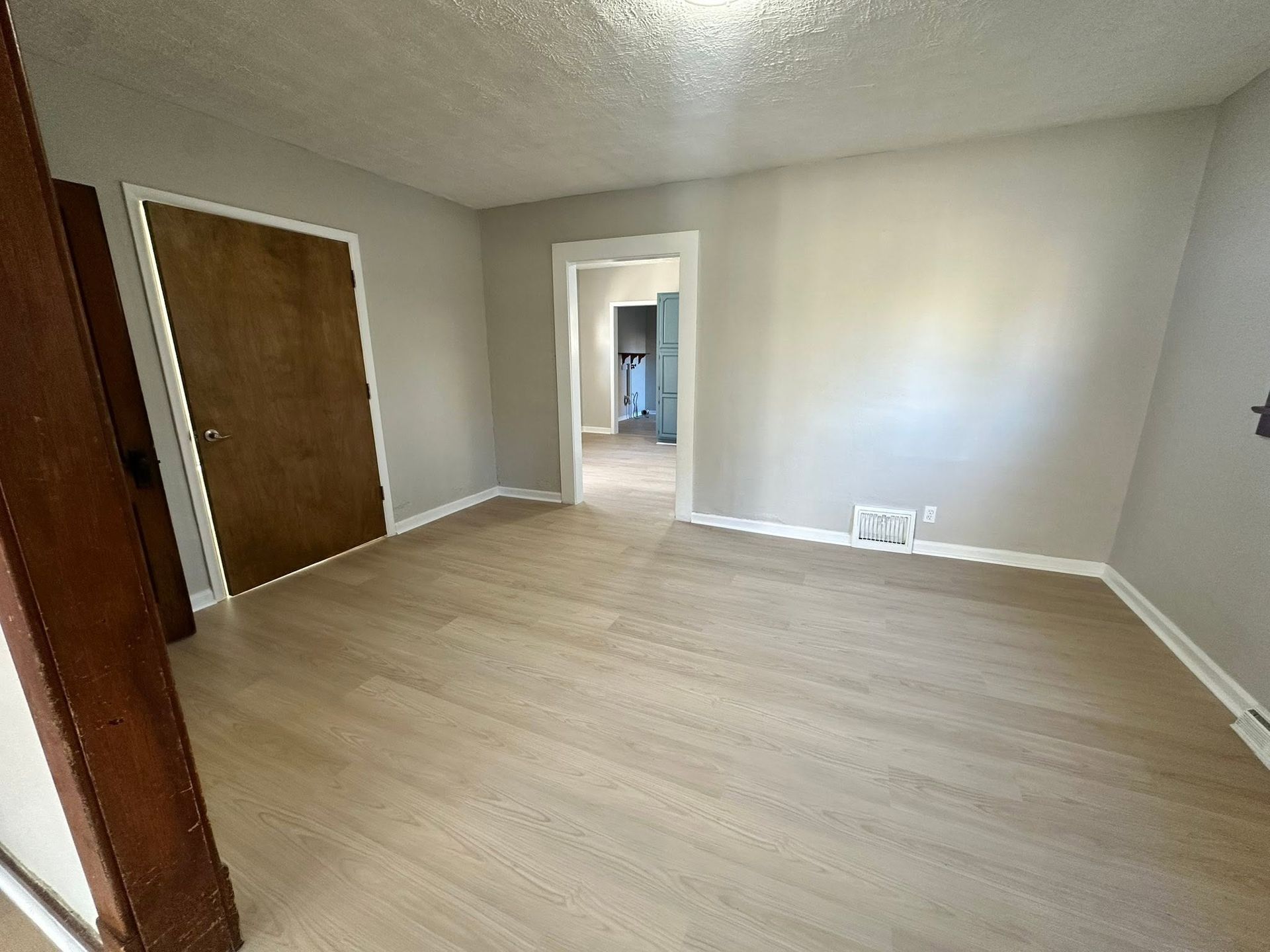 Empty beige room with wood-look flooring, a closet door, and an open doorway to a hallway