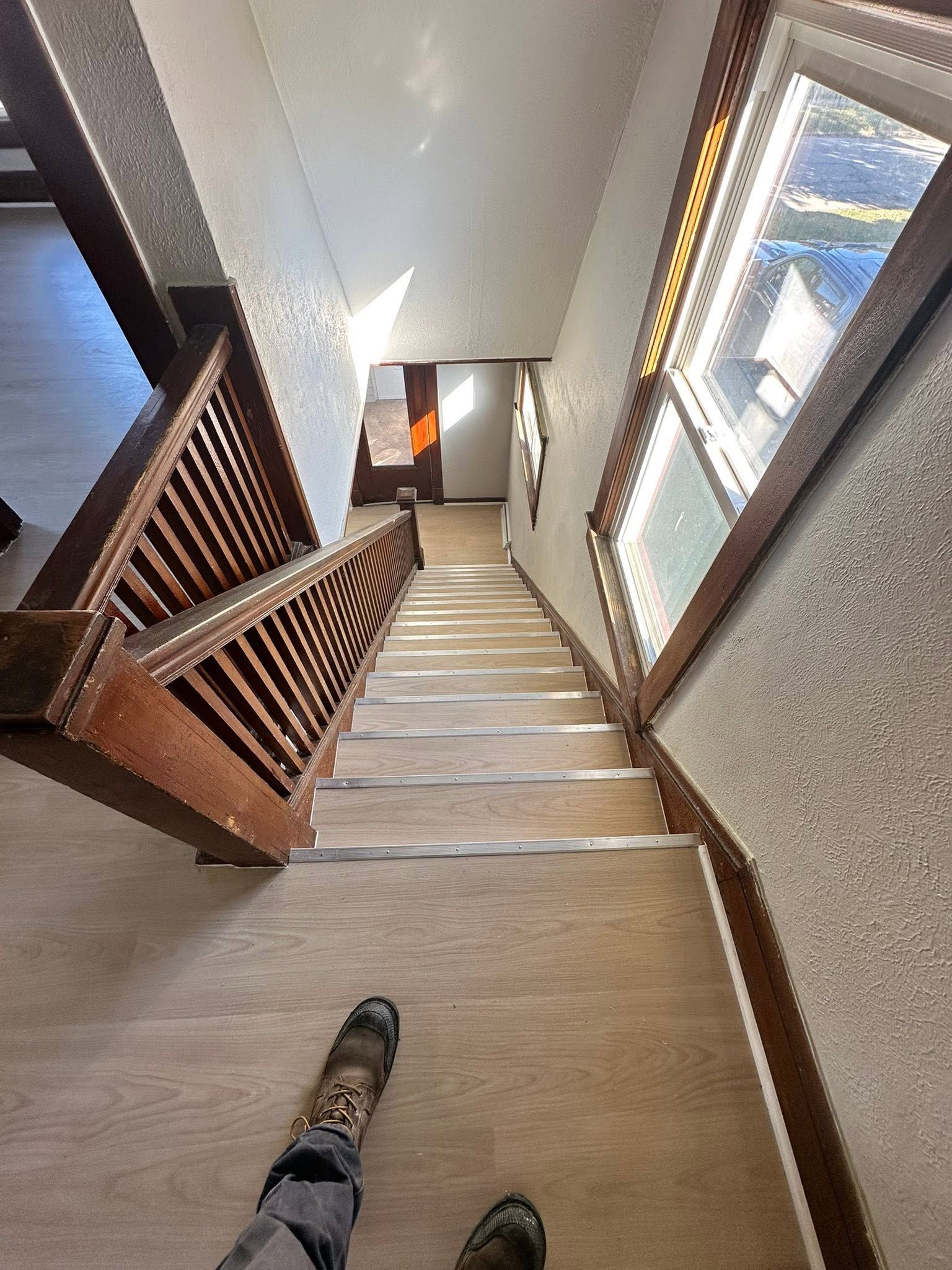 Staircase viewed from above, with wooden banister, carpeted steps, and windows on the right.