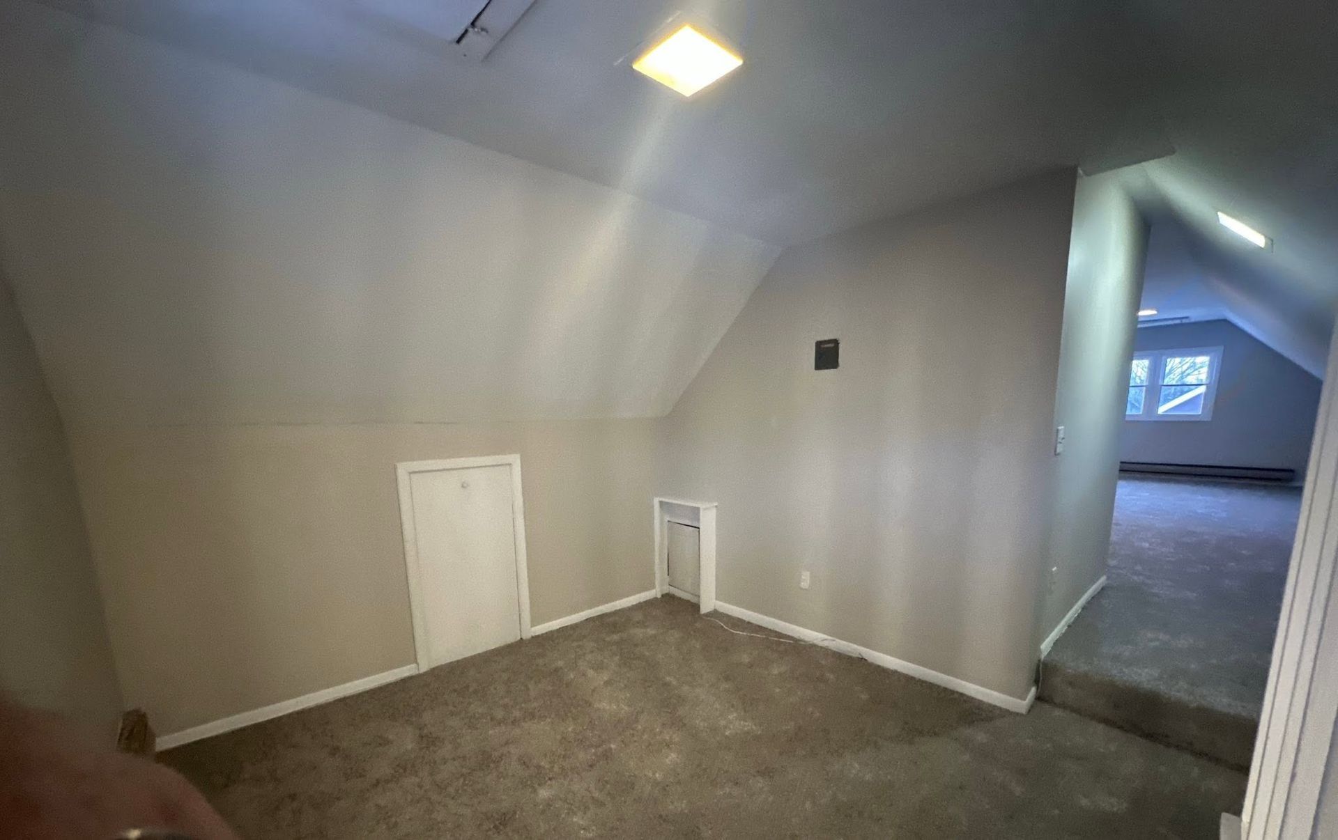 Empty gray carpeted room with sloped ceiling, small closet doors, and a hallway opening to the right