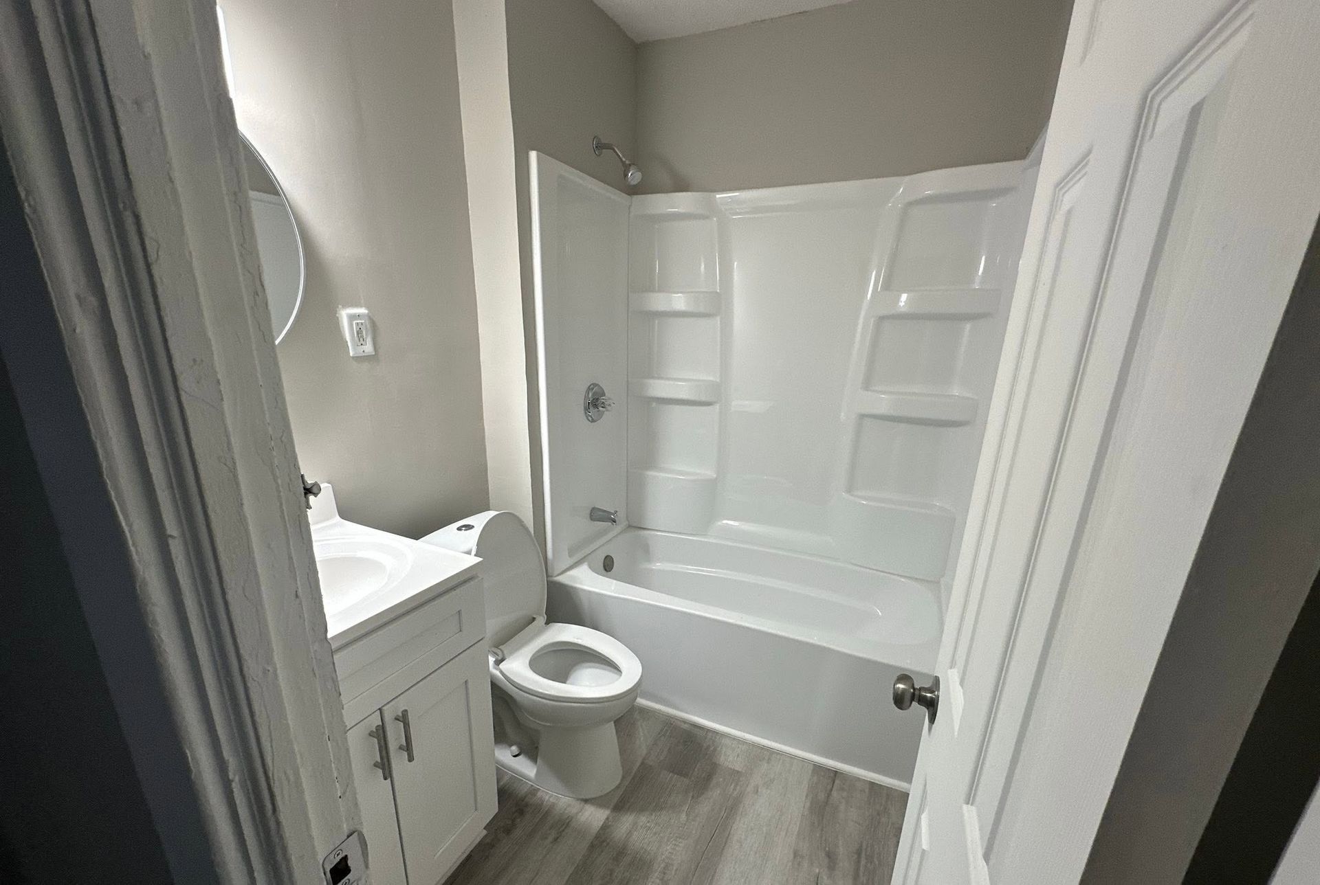 Small bathroom with a toilet, vanity, and white tub-shower combo with built-in shelves.