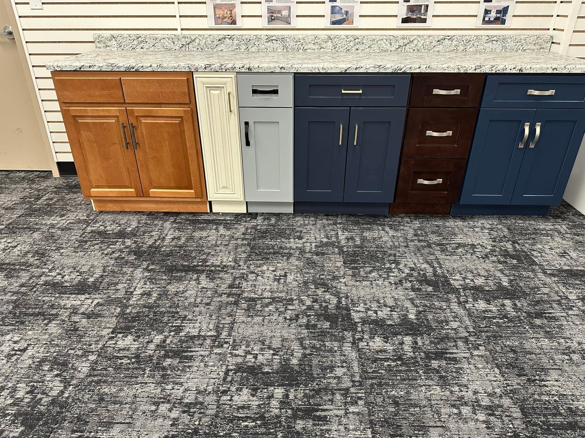 Cabinet display with five sample kitchen cabinets in wood, gray, navy, and dark finishes beneath a countertop