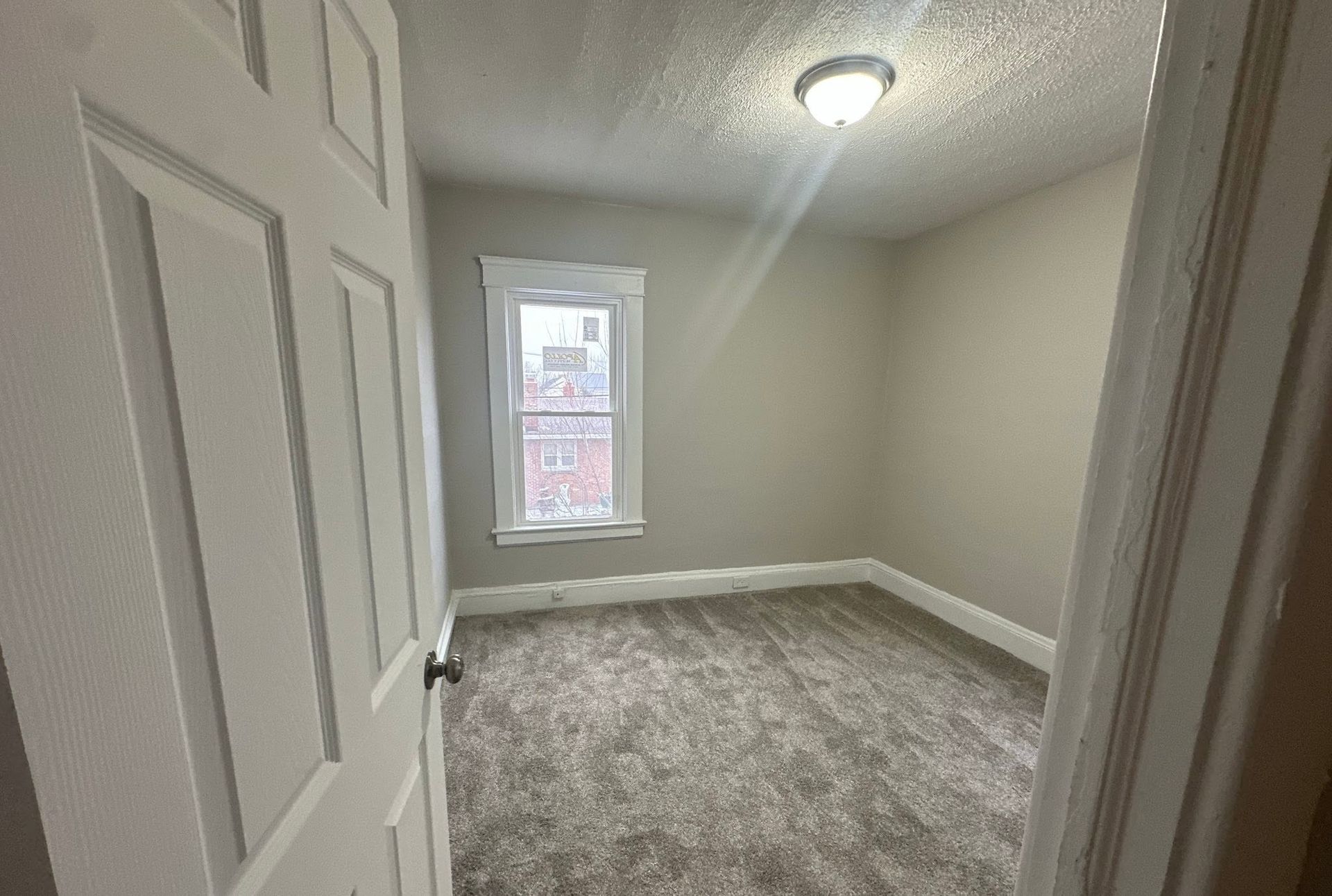 Empty beige bedroom with gray carpet, white trim, and a single window.