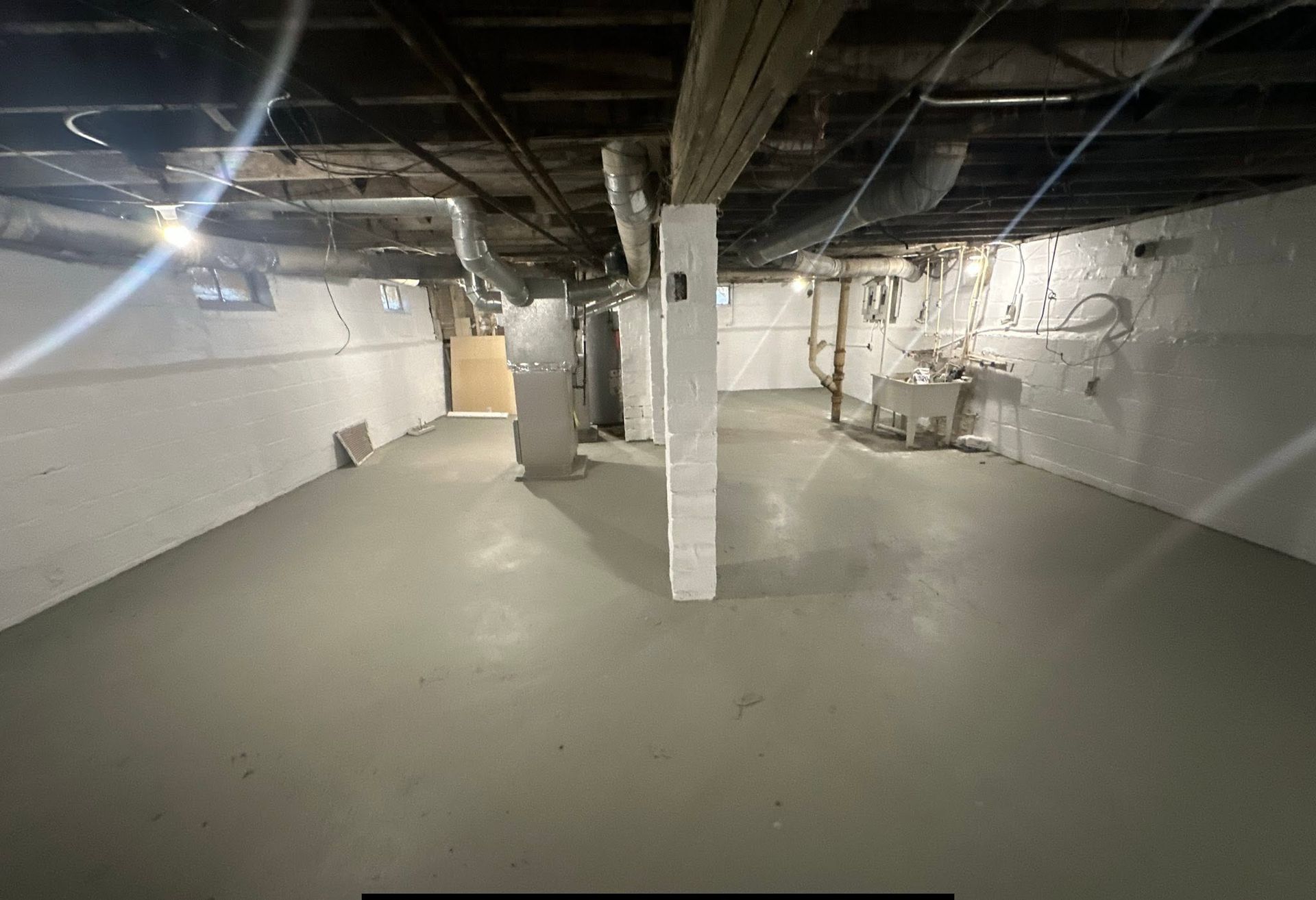 Empty unfinished basement with exposed pipes, white walls, and concrete floor