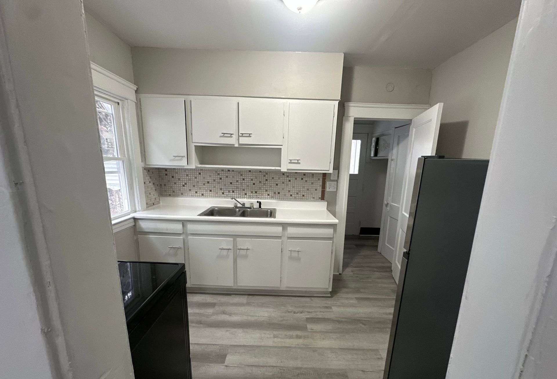 Small white kitchen with cabinets, sink, stove, and gray flooring, viewed from the doorway
