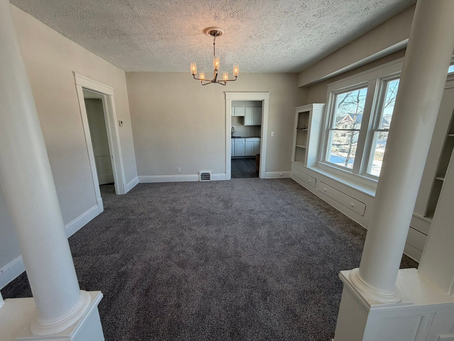 Empty carpeted dining room with white columns, chandelier, and large windows