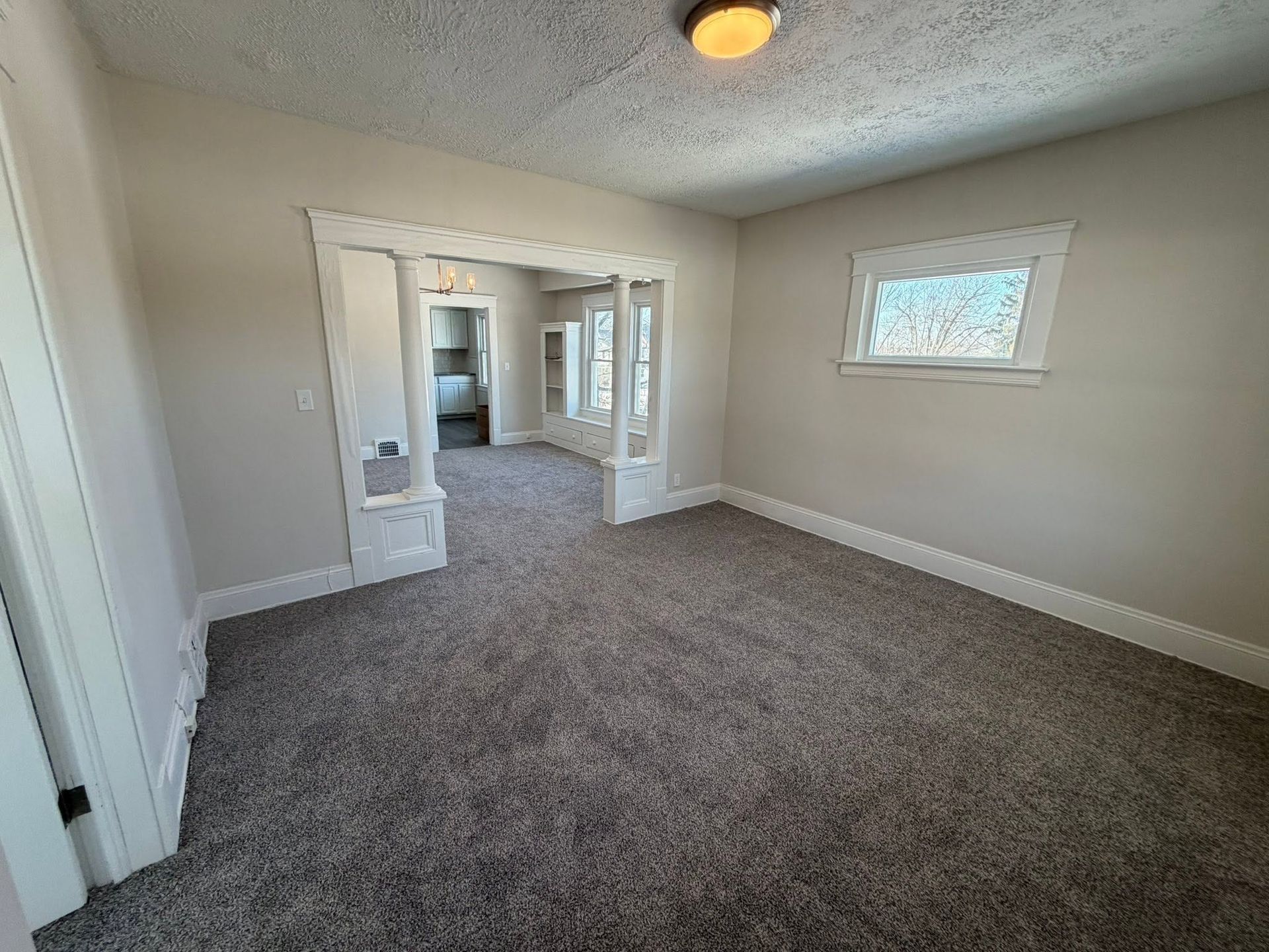 Empty beige bedroom with carpet, closet doors, and a small window.