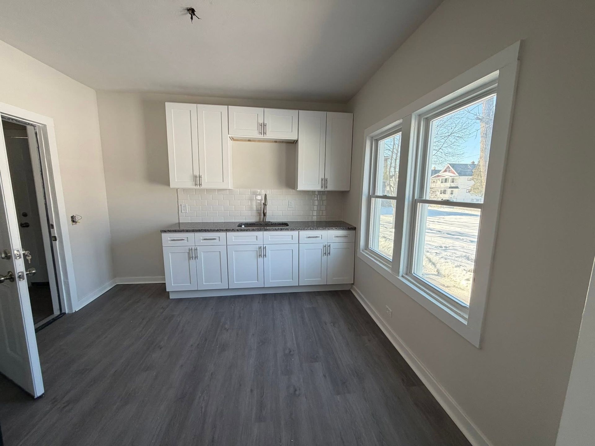 Empty kitchen with white cabinets, gray flooring, and a large window on the right