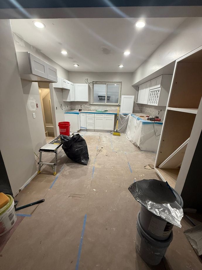 Renovation site with unfinished kitchen, cabinets, tools, debris, and a window at the back.