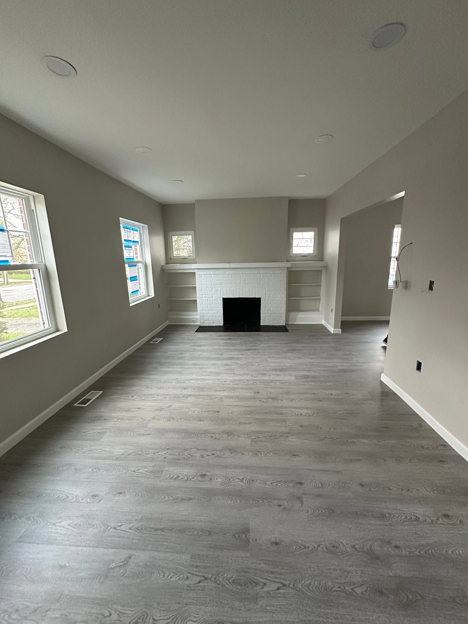 Empty living room with gray floors, white walls, and a fireplace at the far end.
