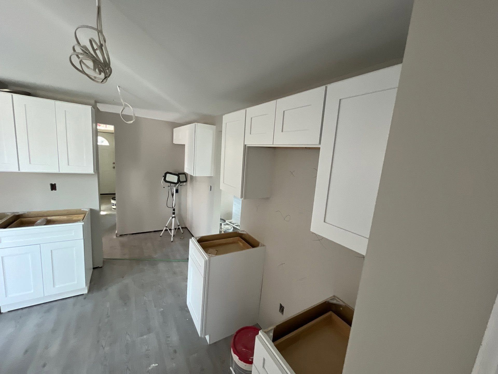 Small white kitchen room with cabinets, gray floor, and a step ladder near the back wall.