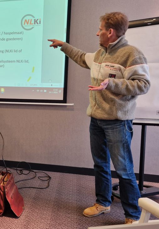 Een presentator wijst naar een geprojecteerde dia in een vergaderzaal.