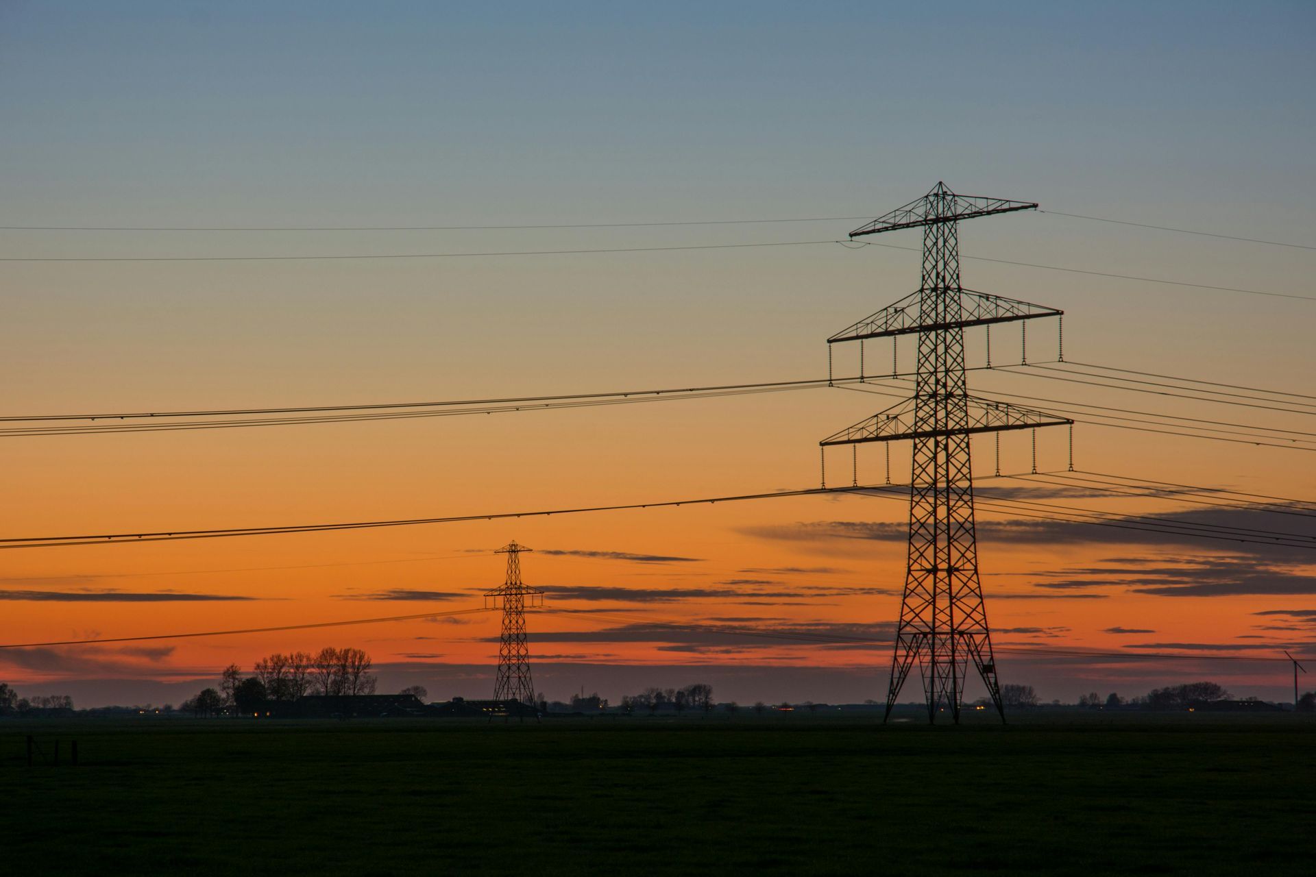 Transmission towers silhouetted against an orange sunset over a flat field