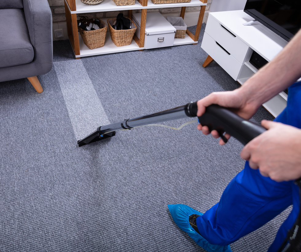 Person vacuuming a gray carpet in a living room with a black handheld vacuum.