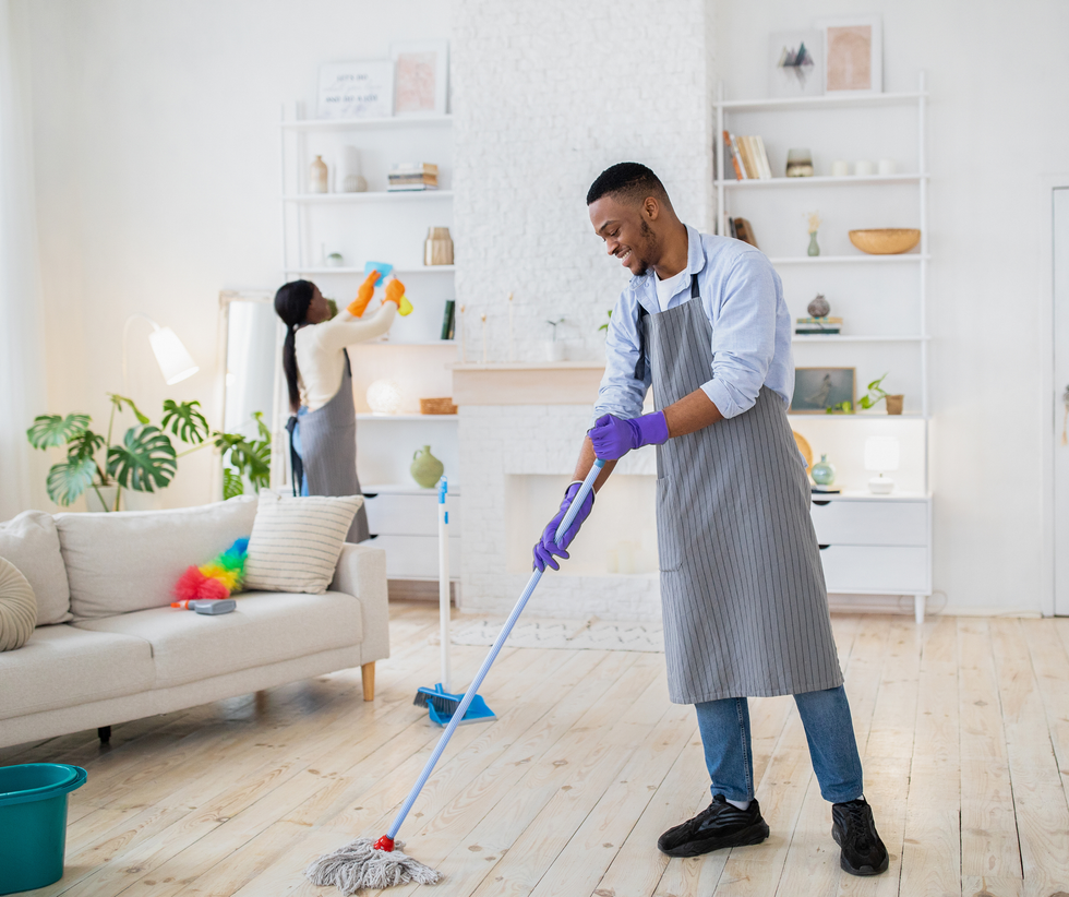 Person mopping a bright living room with a blue mop and purple gloves